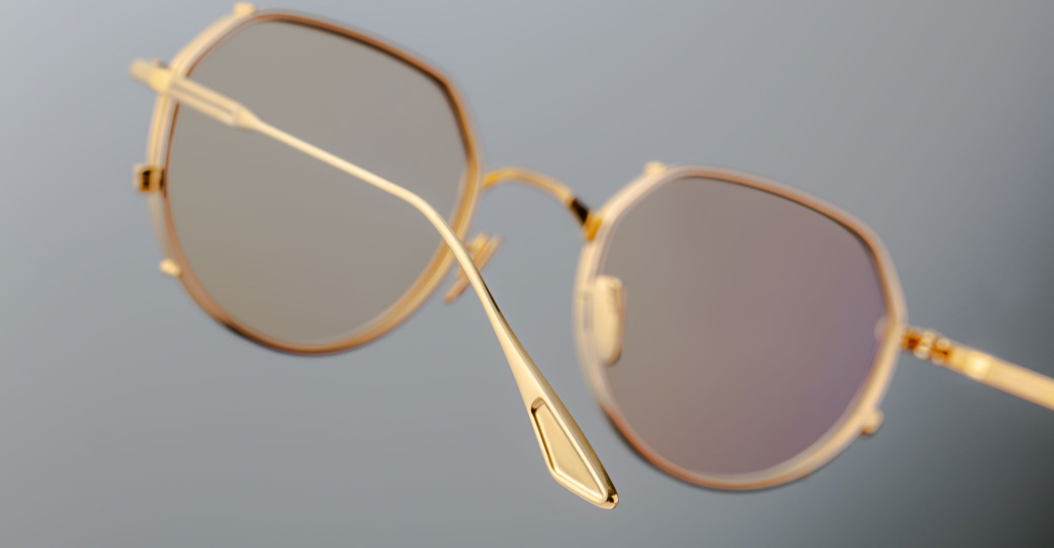 Close-up of Jacques Marie Mage Hartana eyeglasses featuring a gold geometric frame and light-tinted lenses, showcased at an angle that accentuates the thin metal construction against a softly blurred background.