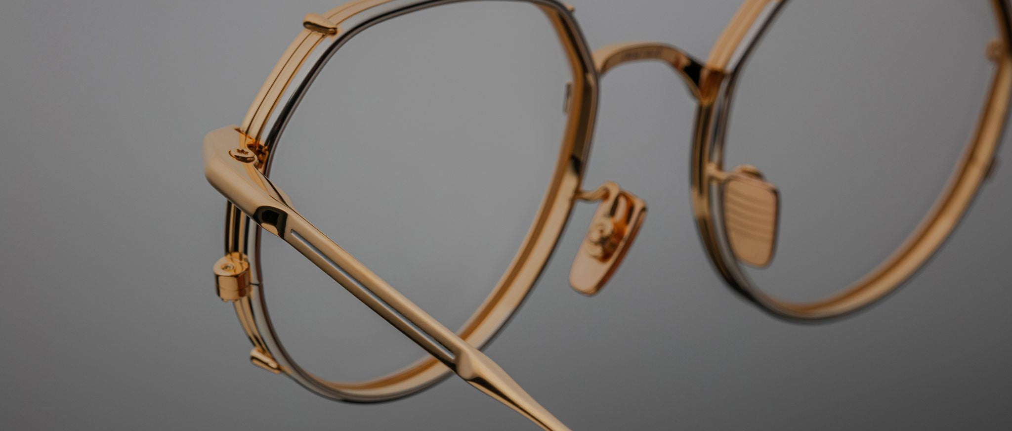 Close-up of Jacques Marie Mage Hartana gold metal eyeglasses with round lenses and adjustable nose pads, displayed against a plain grey background.