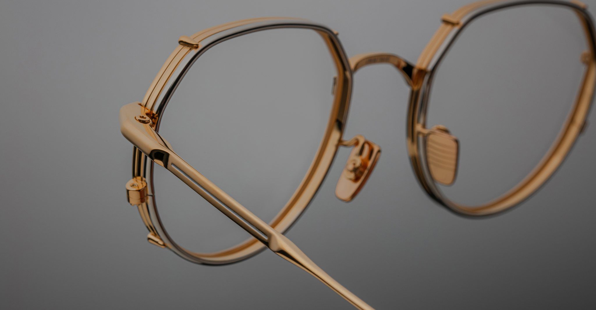 Close-up of Jacques Marie Mage Hartana gold metal eyeglasses with round lenses and adjustable nose pads, displayed against a plain grey background.