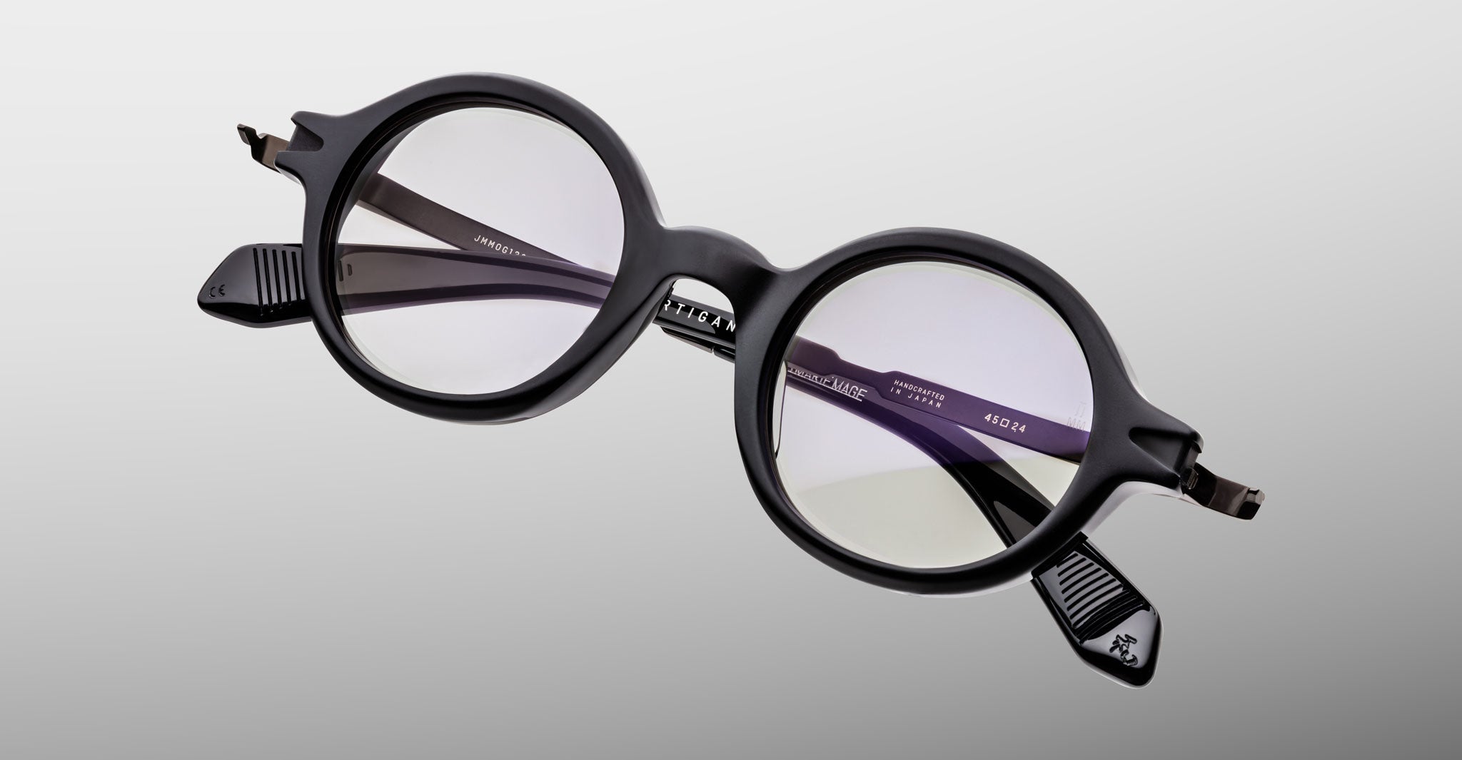Jacques Marie Mage Hartigan in Phantom, round black acetate eyeglasses shown from a close angled front view, featuring a keyhole bridge, exposed metal core temples, and subtle purple anti-reflective lens coating.