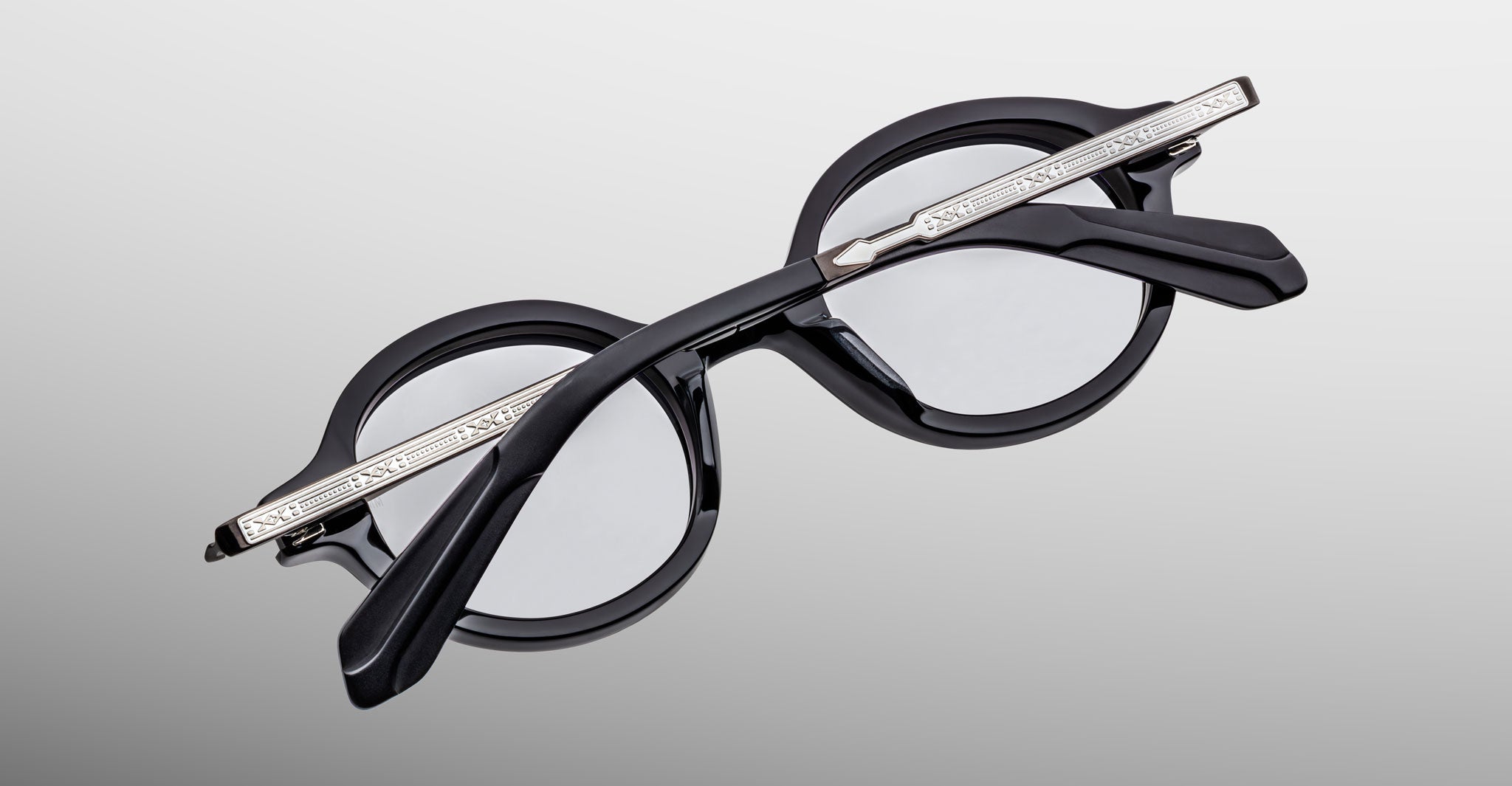 Jacques Marie Mage Hartigan in Phantom, round black acetate eyeglasses shown from an angled top view, highlighting engraved metal core temples, keyhole bridge, and sculpted temple tips with clear demo lenses.