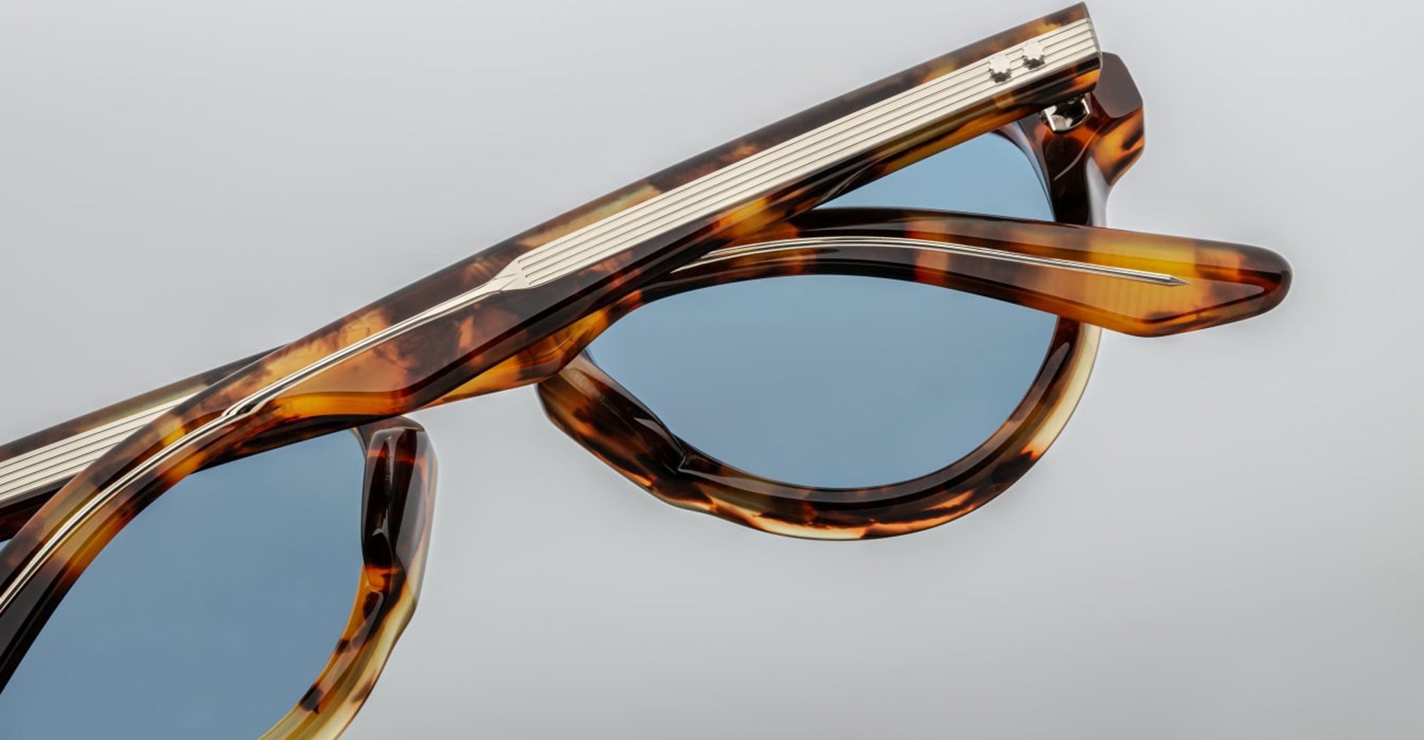 Close-up of Jacques Marie Mage Hatfield tortoiseshell sunglasses with blue-tinted lenses, partially folded, set against a plain light gray background.