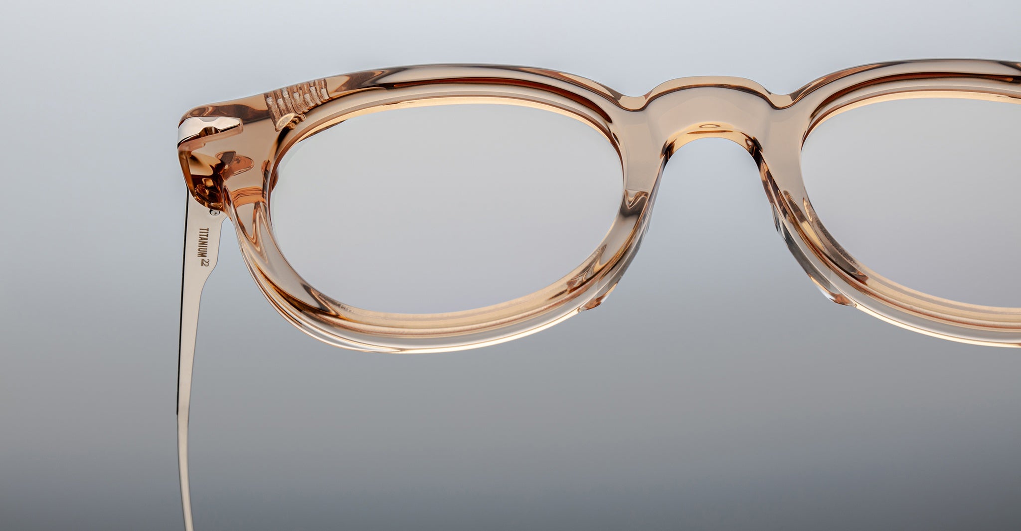 Close-up of the upper half of Jacques Marie Mage Hisao translucent light brown, round eyeglasses, set against a neutral gradient background.