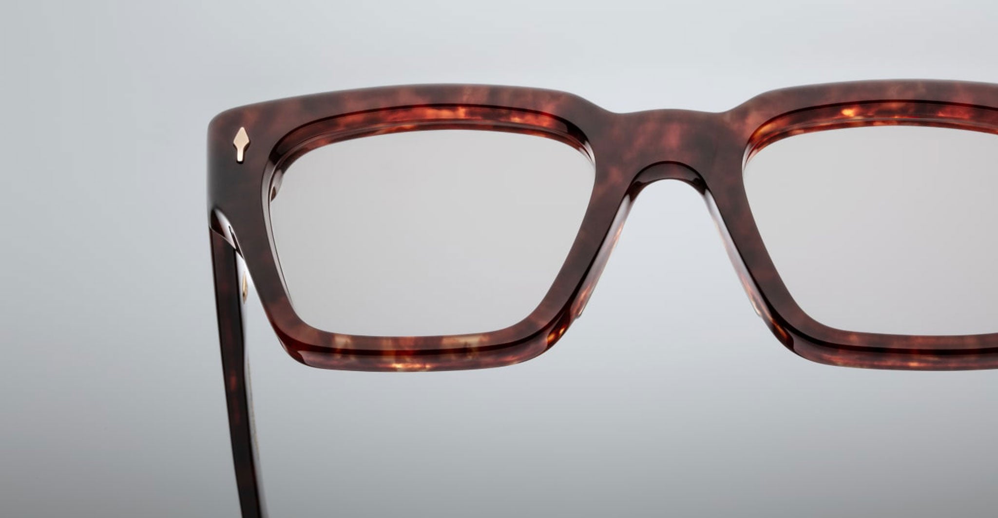 Close-up of the upper half of Jacques Marie Mage Ichikawa rectangular eyeglasses with a dark tortoiseshell frame set against a plain light gray background.