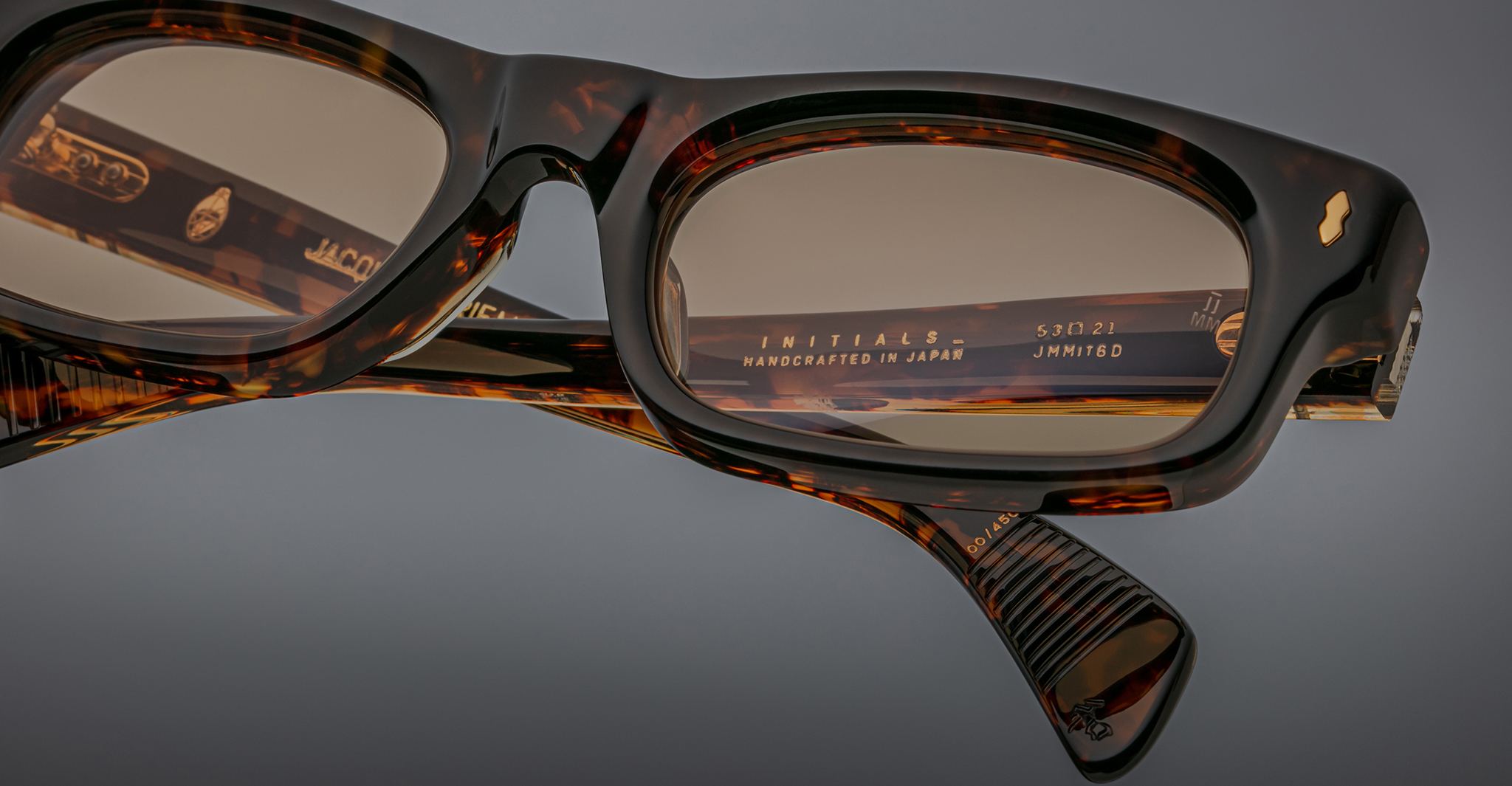 Close-up of Jacques Marie Mage Initials tortoiseshell eyeglasses with rectangular lenses, featuring handcrafted details and limited-edition text on the frame, made in Japan.