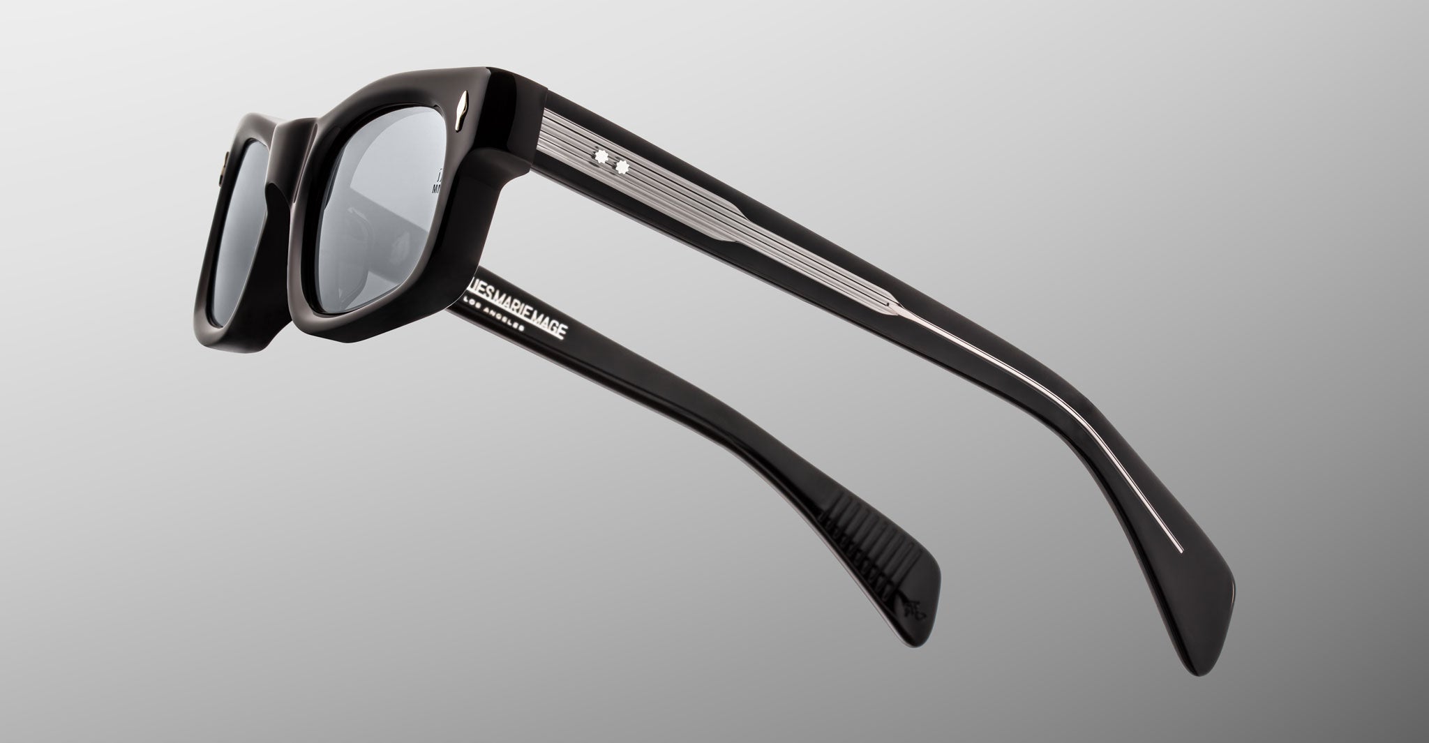 Jacques Marie Mage Initials: Black rectangular micro-frame sunglasses featuring gray temples, dark lenses, and detailed arms, showcased on a plain gradient background—part of Jacques Marie Mage's limited-edition collection.