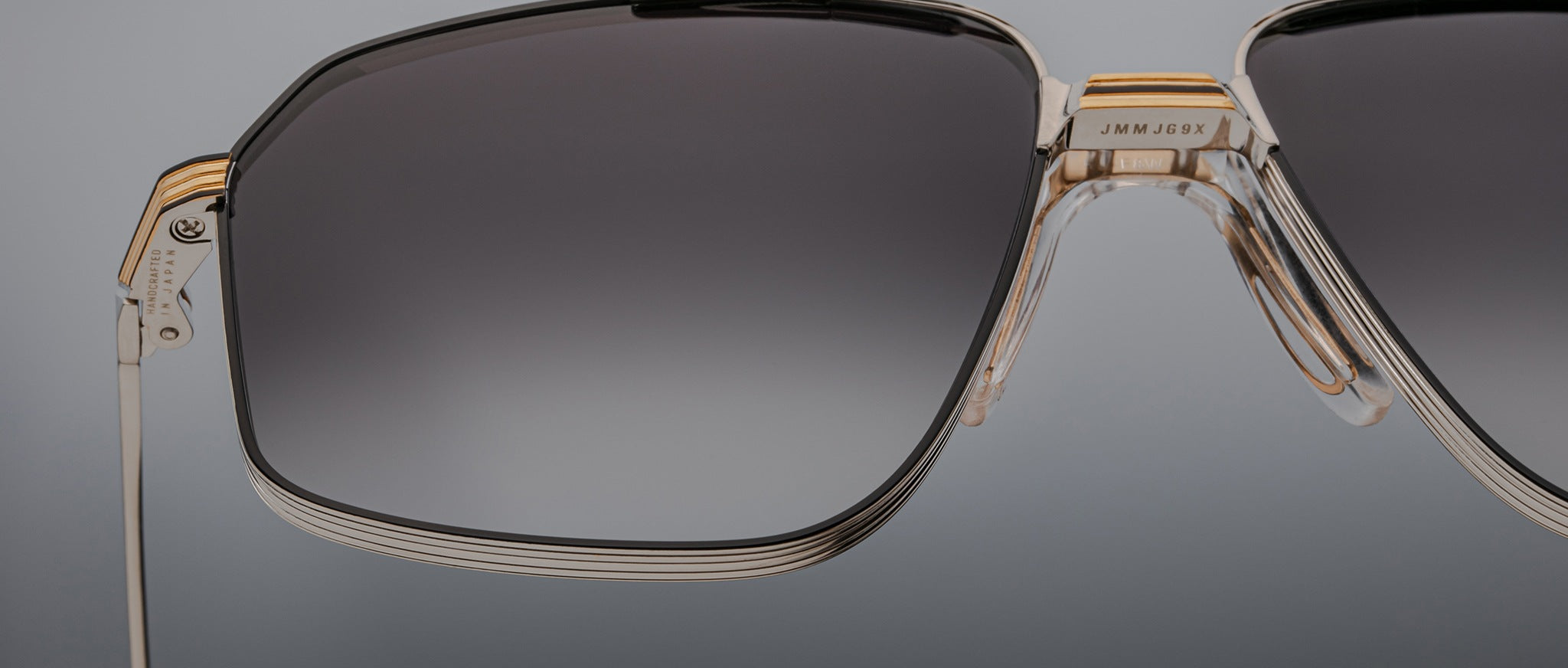 Close-up of the left side of Jacques Marie Mage’s Jagger oversized aviator sunglasses, featuring a metal frame, gradient-tinted lenses, and gold accents against a neutral backdrop.