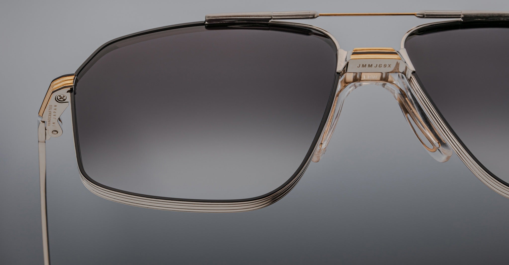 Close-up of the left side of Jacques Marie Mage’s Jagger oversized aviator sunglasses, featuring a metal frame, gradient-tinted lenses, and gold accents against a neutral backdrop.