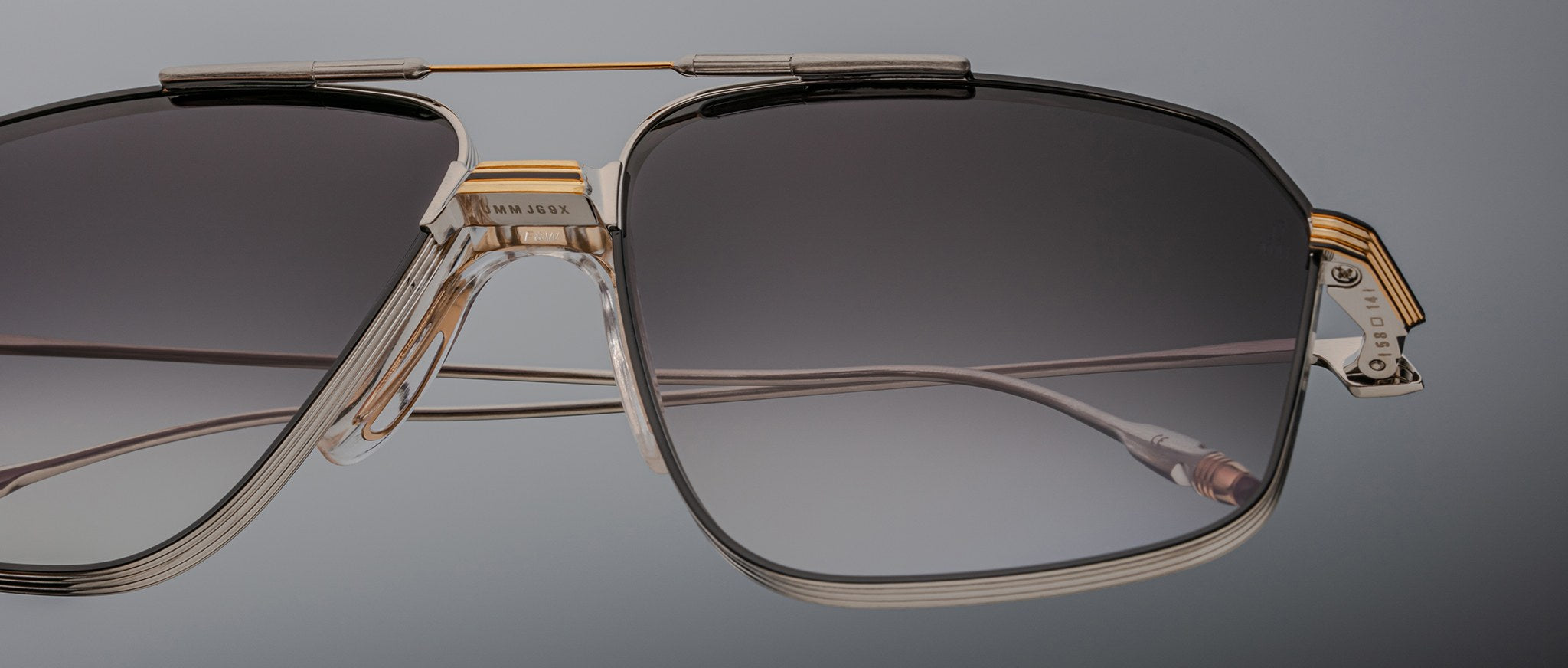 Close-up of Jacques Marie Mage Jagger oversized aviator sunglasses by Jacques Marie Mage, featuring black gradient lenses, a beta titanium bridge, and gold accents against a plain background.