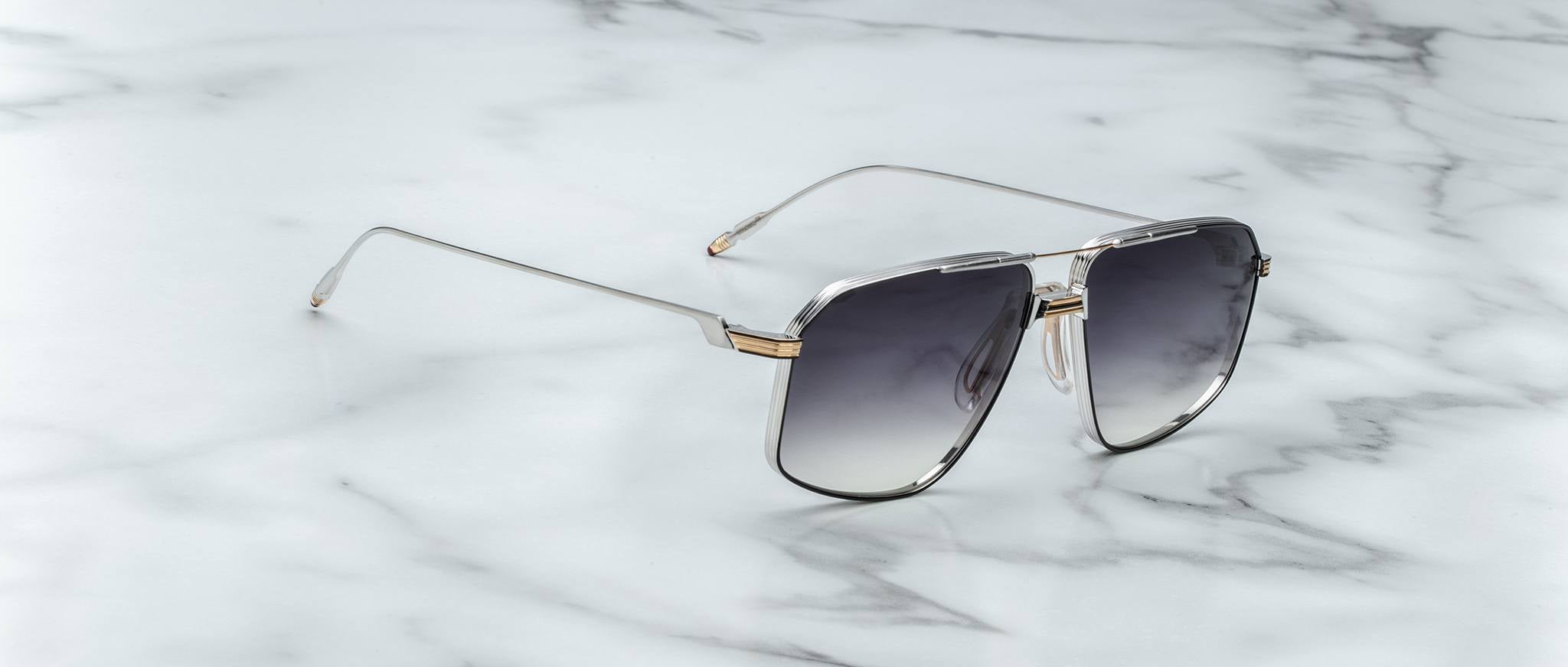 The Jacques Marie Mage Jagger sunglasses, featuring oversized aviator frames in silver beta titanium with gradient dark lenses, are displayed on a white marble surface.