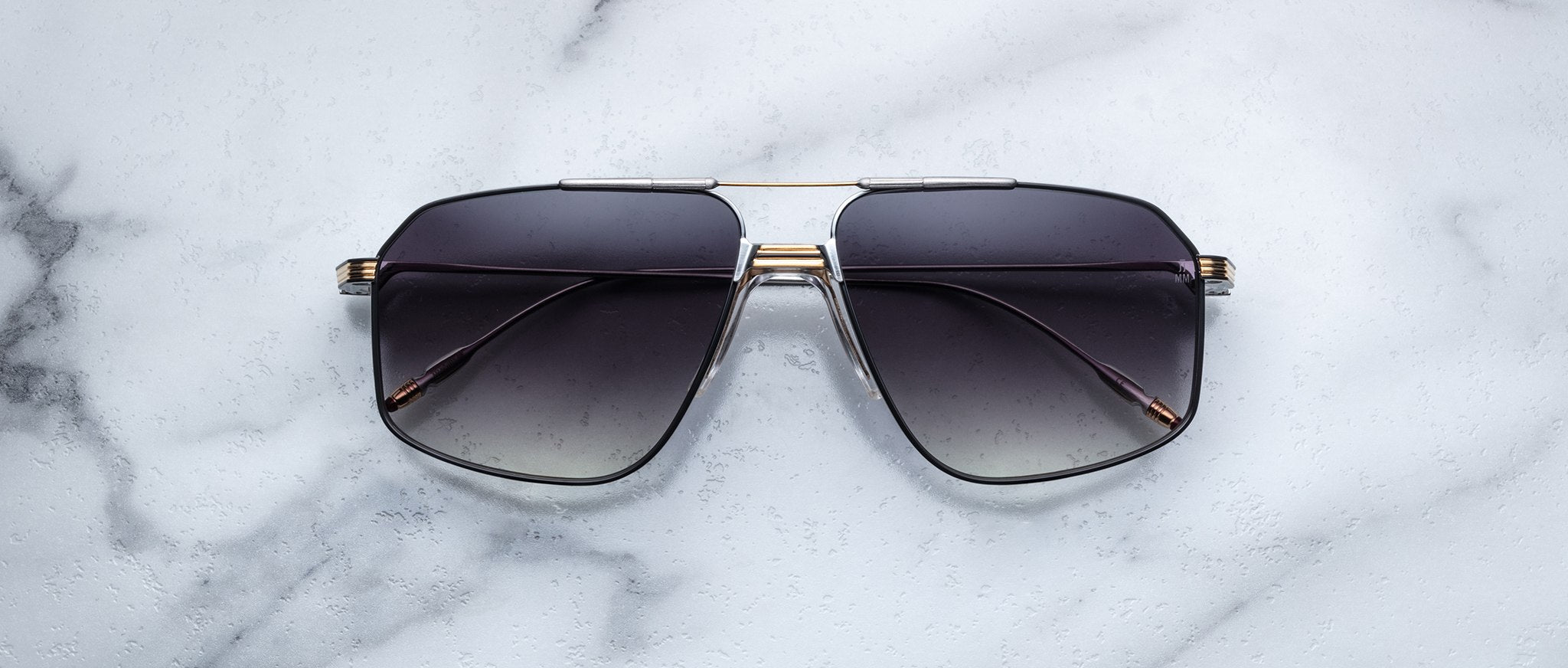 A pair of dark, oversized Jacques Marie Mage Jagger aviator sunglasses with thin beta titanium frames by Jacques Marie Mage, shown on a white marble surface.