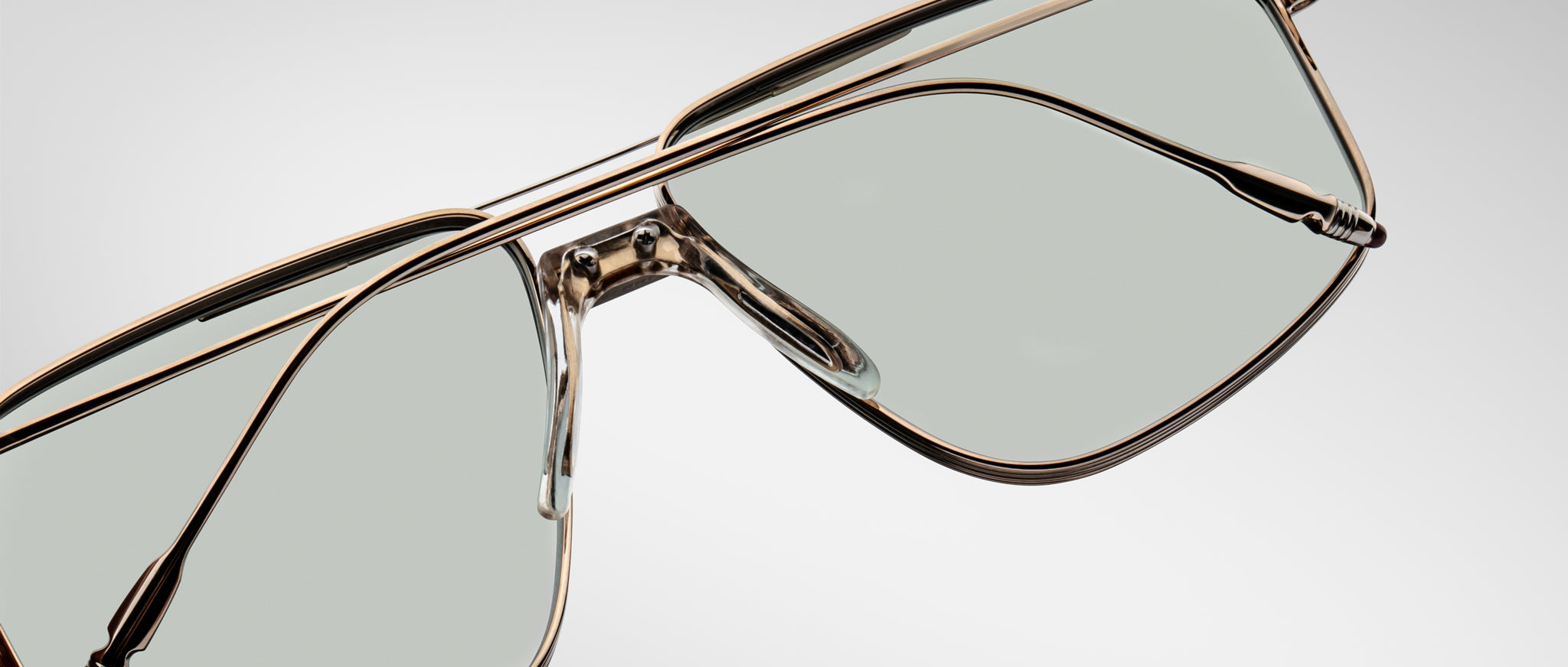 Close-up of Jacques Marie Mage Jagger oversized aviator sunglasses by Jacques Marie Mage, showcasing gold metal frames, beta titanium accents, clear nose pads, and light gray tinted lenses against a plain background.