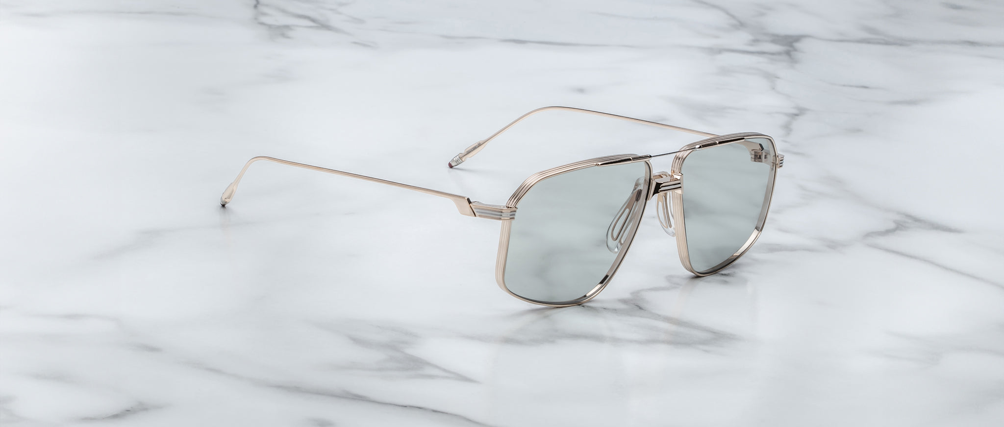 The Jacques Marie Mage Jagger oversized aviator sunglasses feature reflective lenses and a silver beta titanium frame, displayed on a white marble surface.