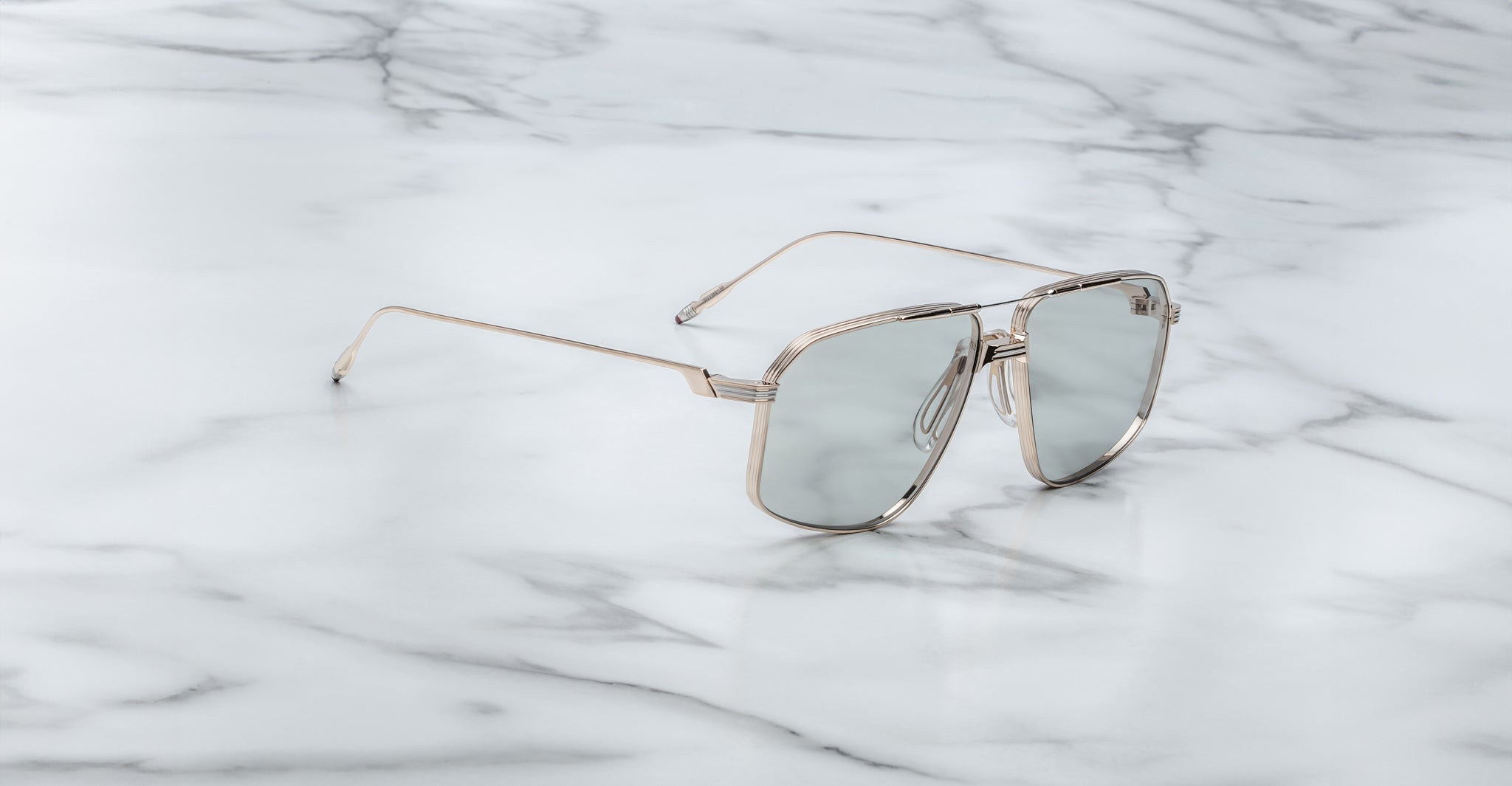 The Jacques Marie Mage Jagger oversized aviator sunglasses feature reflective lenses and a silver beta titanium frame, displayed on a white marble surface.