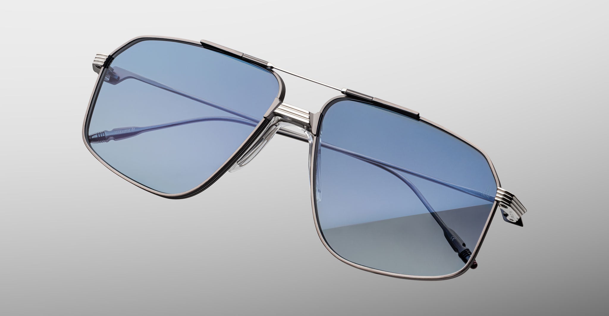 Close-up of Jacques Marie Mage Jagger oversized aviator sunglasses with blue-tinted lenses and metal frames, set against a plain gradient grey background.
