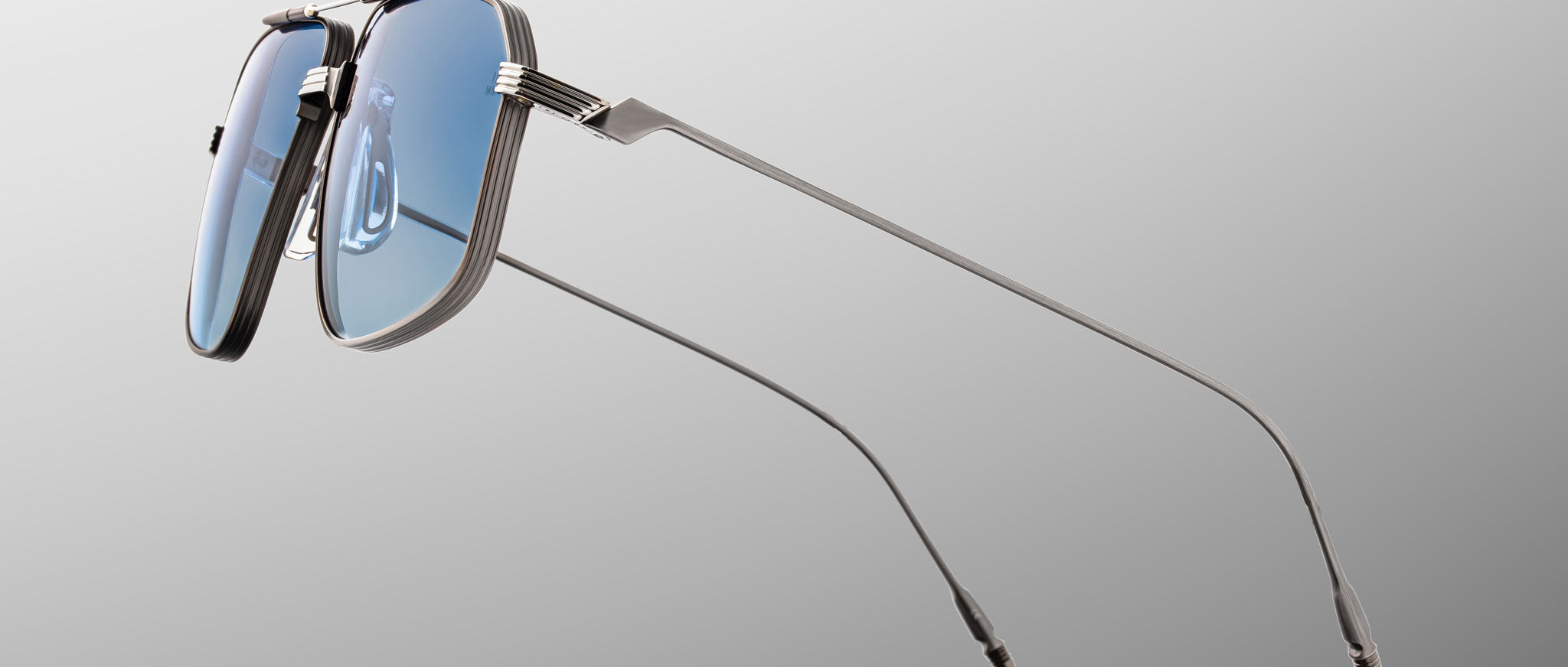 A pair of Jacques Marie Mage Jagger oversized aviator sunglasses, featuring silver frames and blue-tinted lenses, is displayed from a side angle on a light gray background.