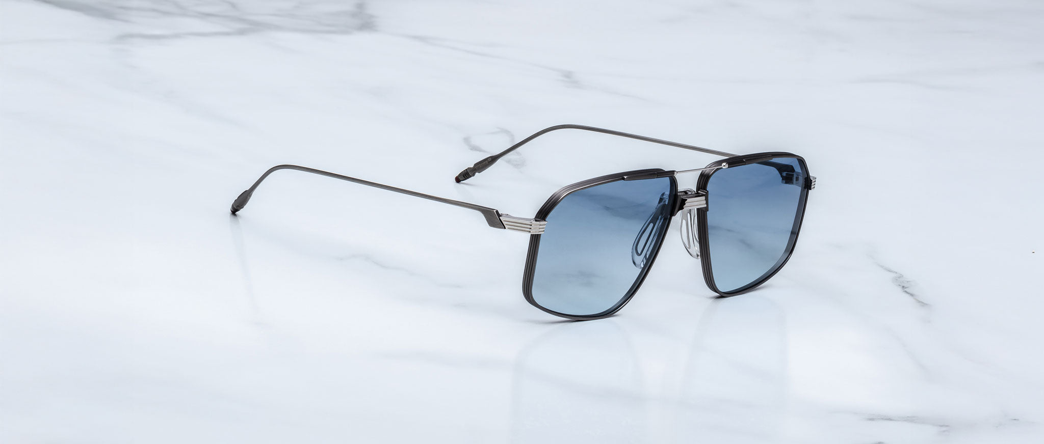 The Jacques Marie Mage Jagger oversized aviator sunglasses with blue tinted lenses from Jacques Marie Mage rest elegantly on a white marble surface.
