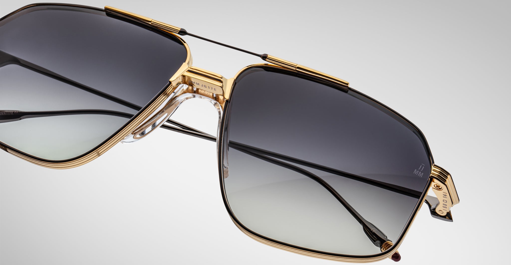 Close-up of Jacques Marie Mage Jagger sunglasses by Jacques Marie Mage, showcasing oversized aviator style with gold beta titanium frames and gradient gray lenses against a plain background.