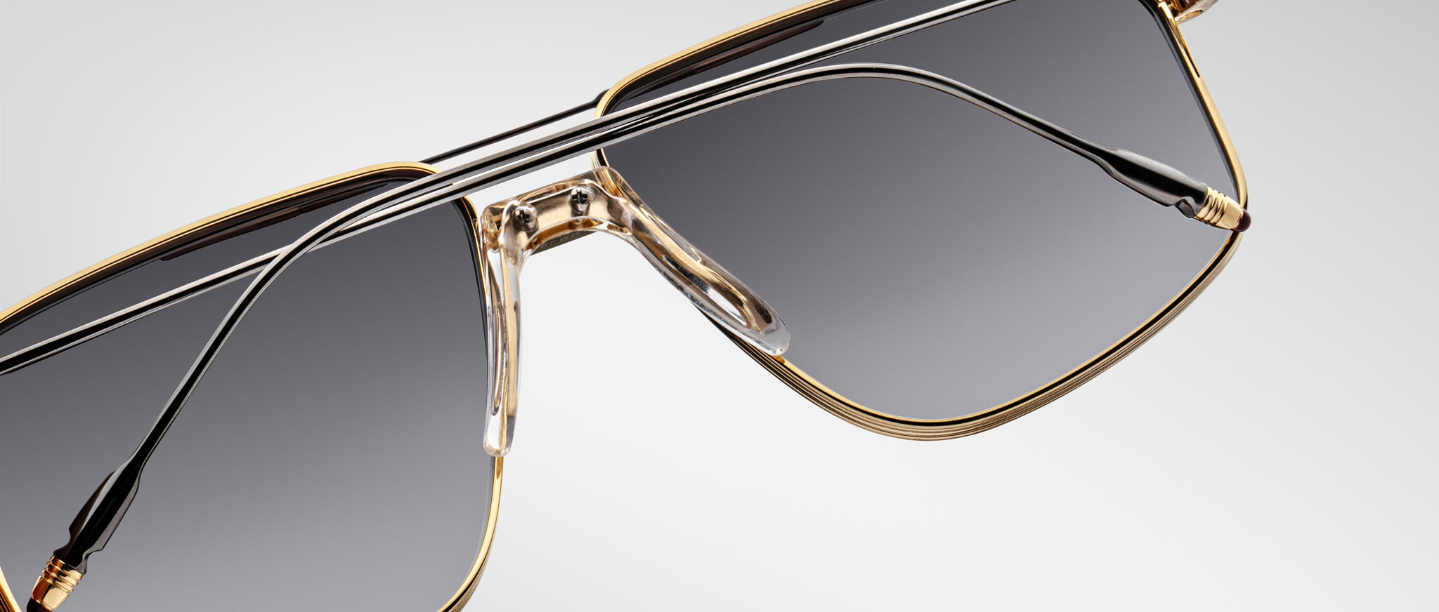 Close-up of Jacques Marie Mage Jagger sunglasses by Jacques Marie Mage, showcasing oversized aviator style with gold rims, dark tinted lenses, and sleek black temples against a light background.
