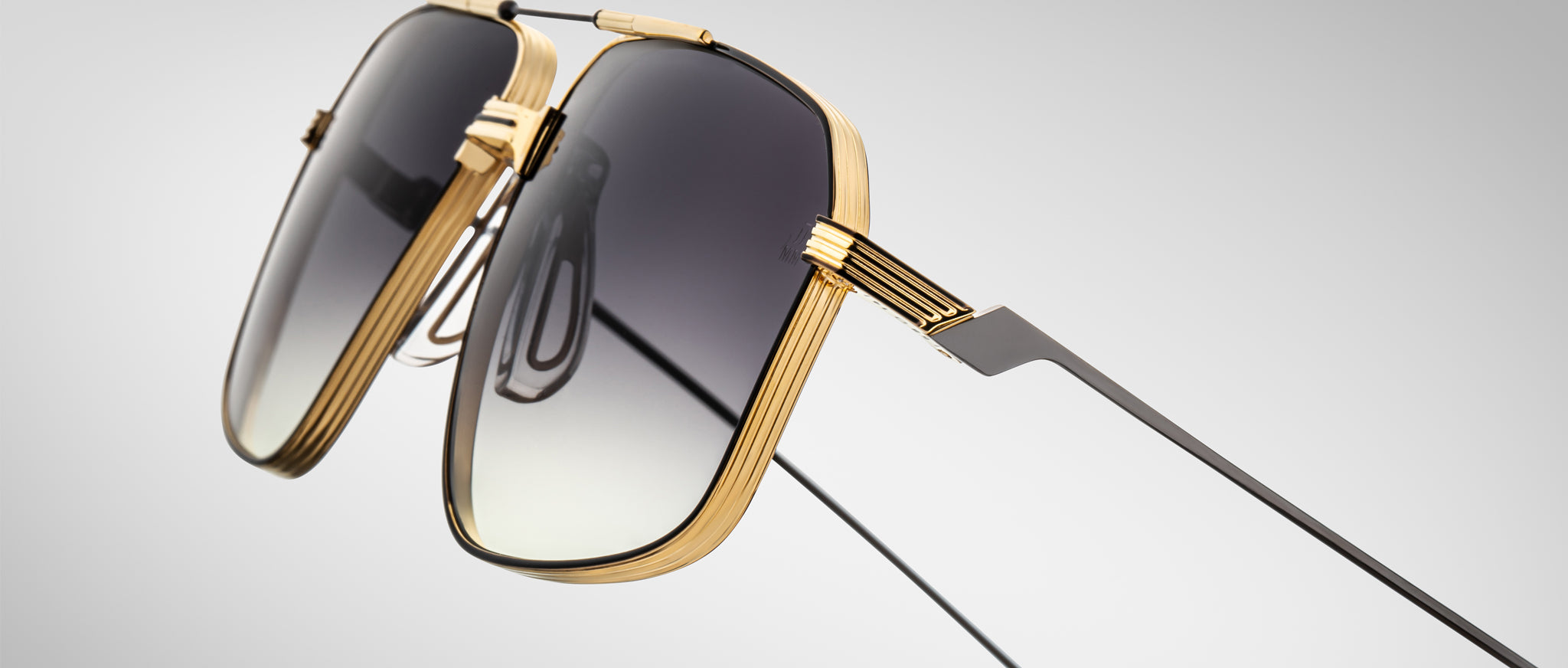 Close-up of Jacques Marie Mage Jagger oversized aviator sunglasses by Jacques Marie Mage, featuring gold beta titanium frames and dark gradient lenses, set against a plain light gray background.