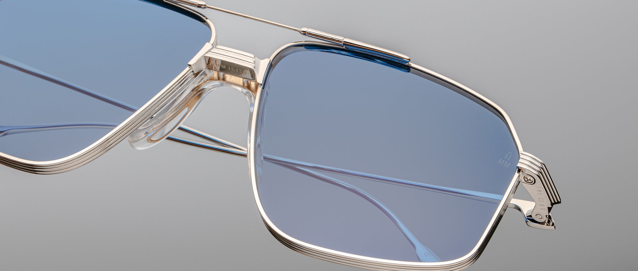Close-up of the Jacques Marie Mage Jagger sunglasses by Jacques Marie Mage, featuring oversized aviator frames in silver beta titanium and blue-tinted lenses, highlighting their intricate design against a neutral background.