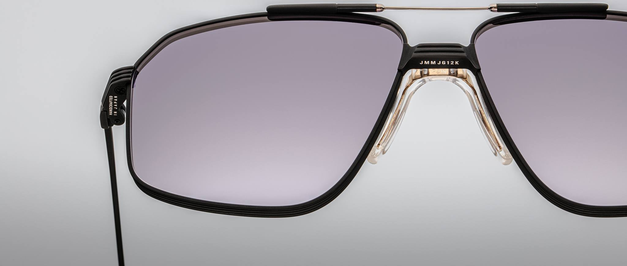 Close-up of Jacques Marie Mage Jagger oversized aviator sunglasses featuring black rims, light purple-tinted lenses, a double beta titanium bridge, and a black cord attached to the left temple.