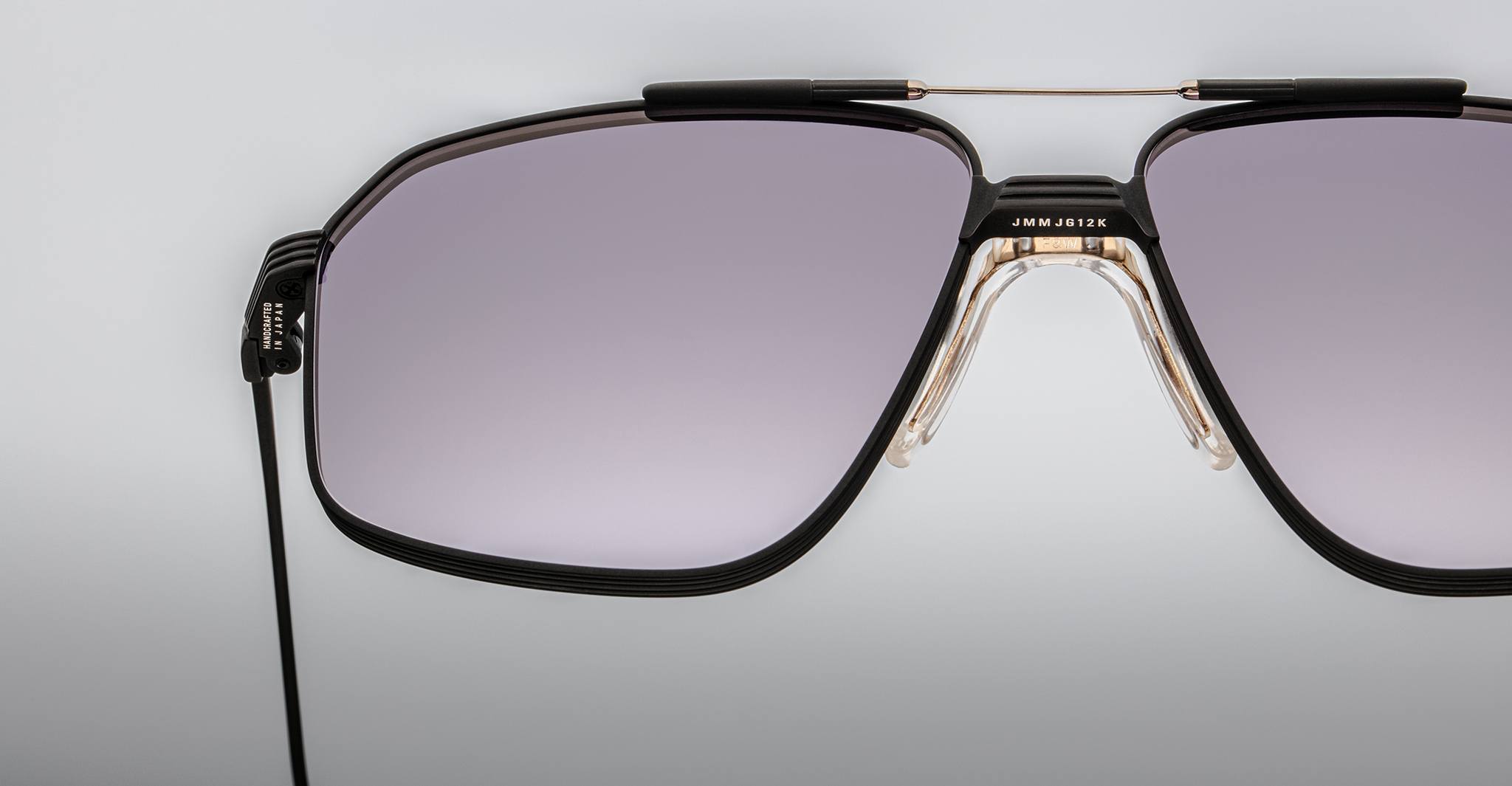 Close-up of Jacques Marie Mage Jagger oversized aviator sunglasses featuring black rims, light purple-tinted lenses, a double beta titanium bridge, and a black cord attached to the left temple.