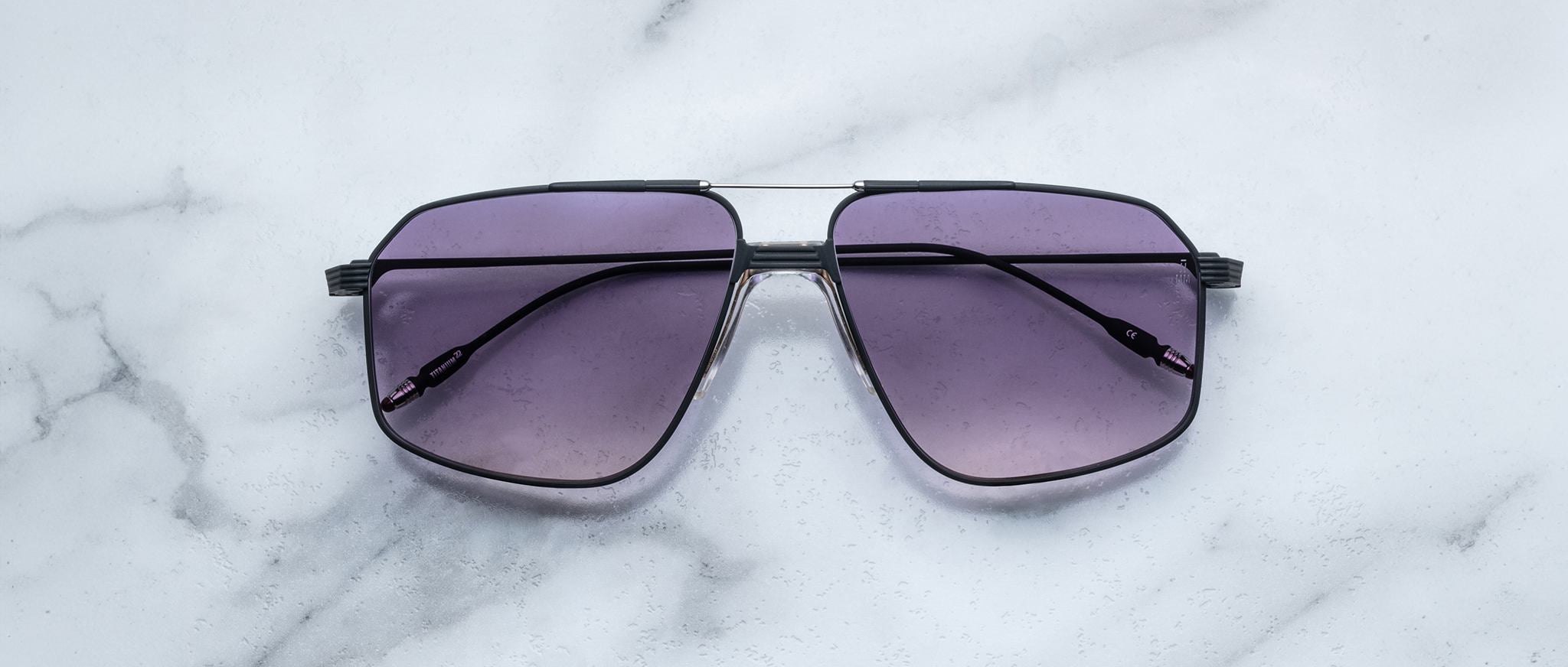 Jacques Marie Mage Jagger oversized aviator sunglasses by Jacques Marie Mage, with black frames and purple-tinted lenses, displayed on a white marble surface.