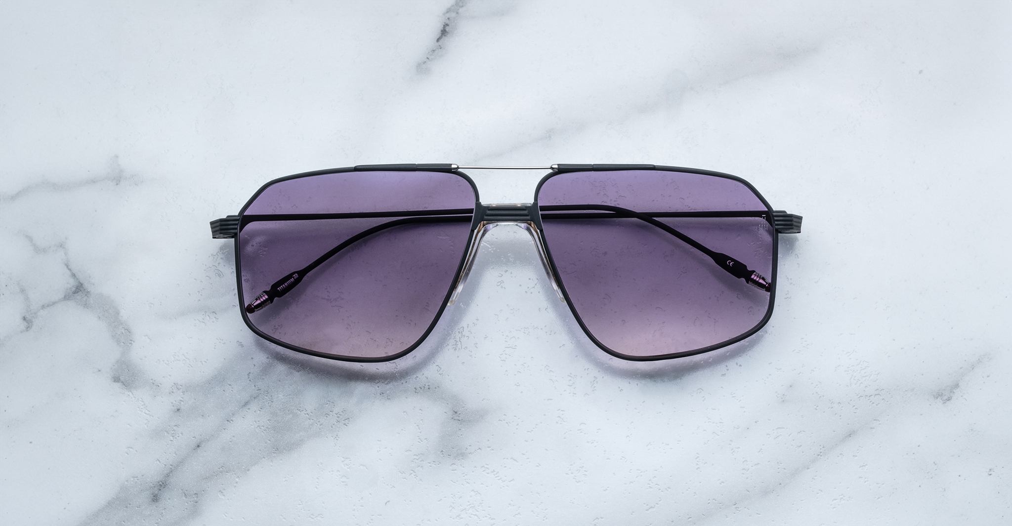 Jacques Marie Mage Jagger oversized aviator sunglasses by Jacques Marie Mage, with black frames and purple-tinted lenses, displayed on a white marble surface.