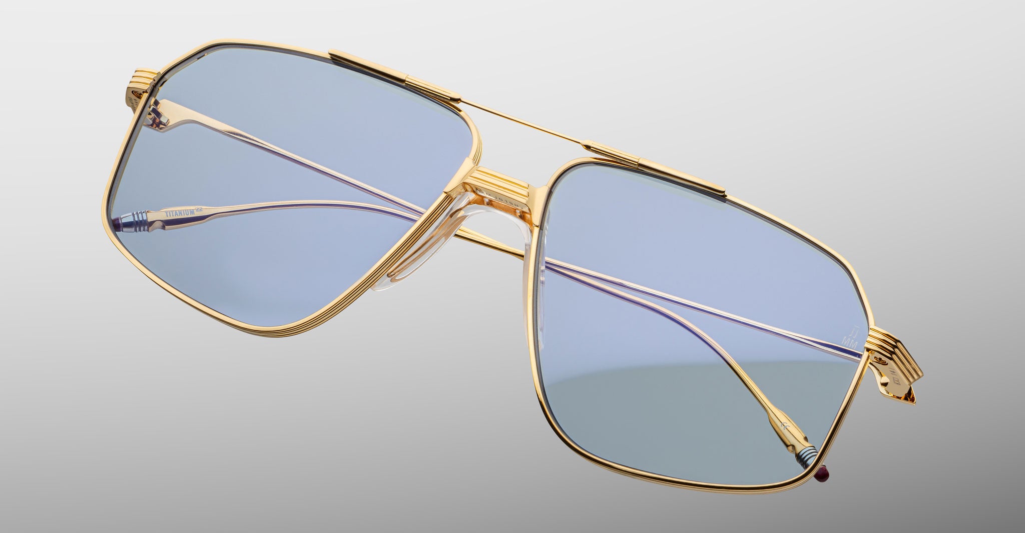 Jacques Marie Mage Jagger gold-framed oversized aviator sunglasses with blue-tinted lenses by Jacques Marie Mage, displayed on a light gray background.