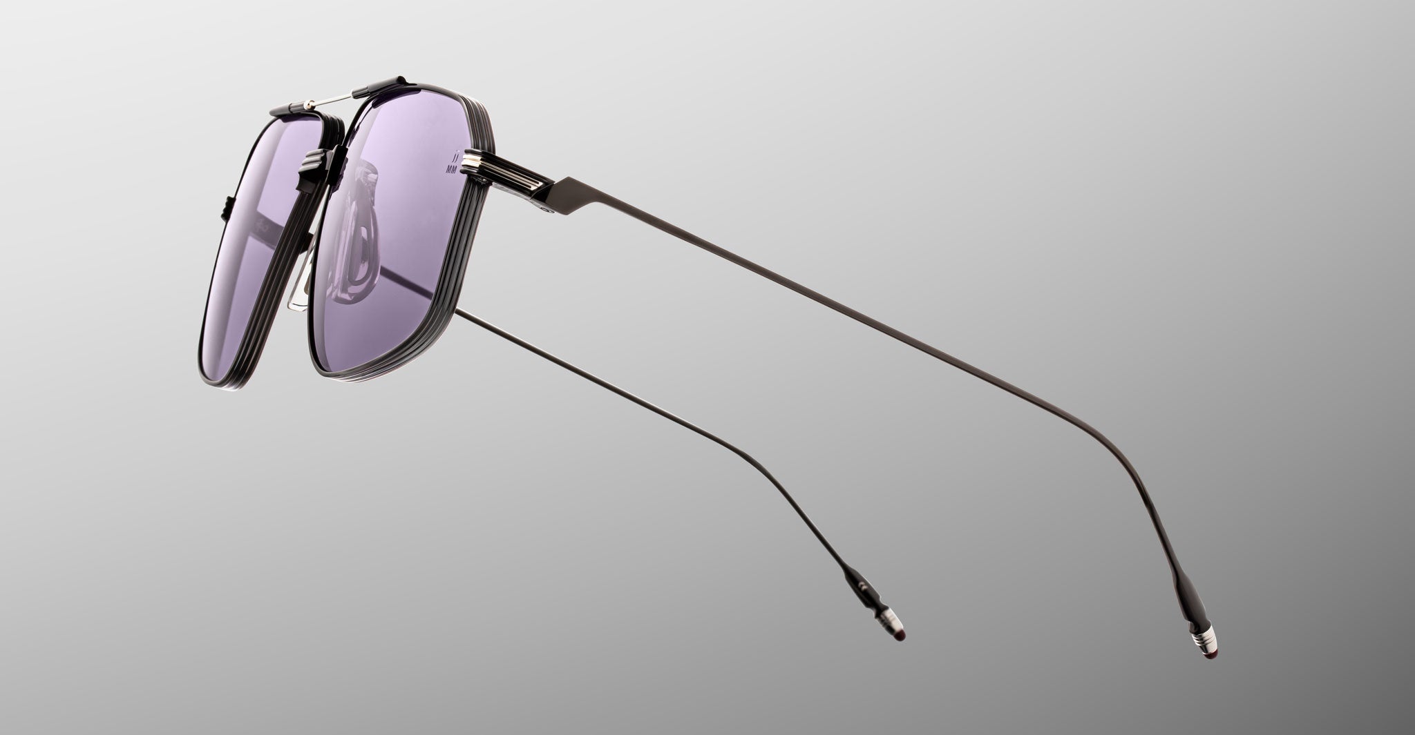 The Jacques Marie Mage Jagger sunglasses by Jacques Marie Mage feature modern oversized aviator frames in thin black beta titanium with purple-tinted lenses, displayed against a plain gray background.