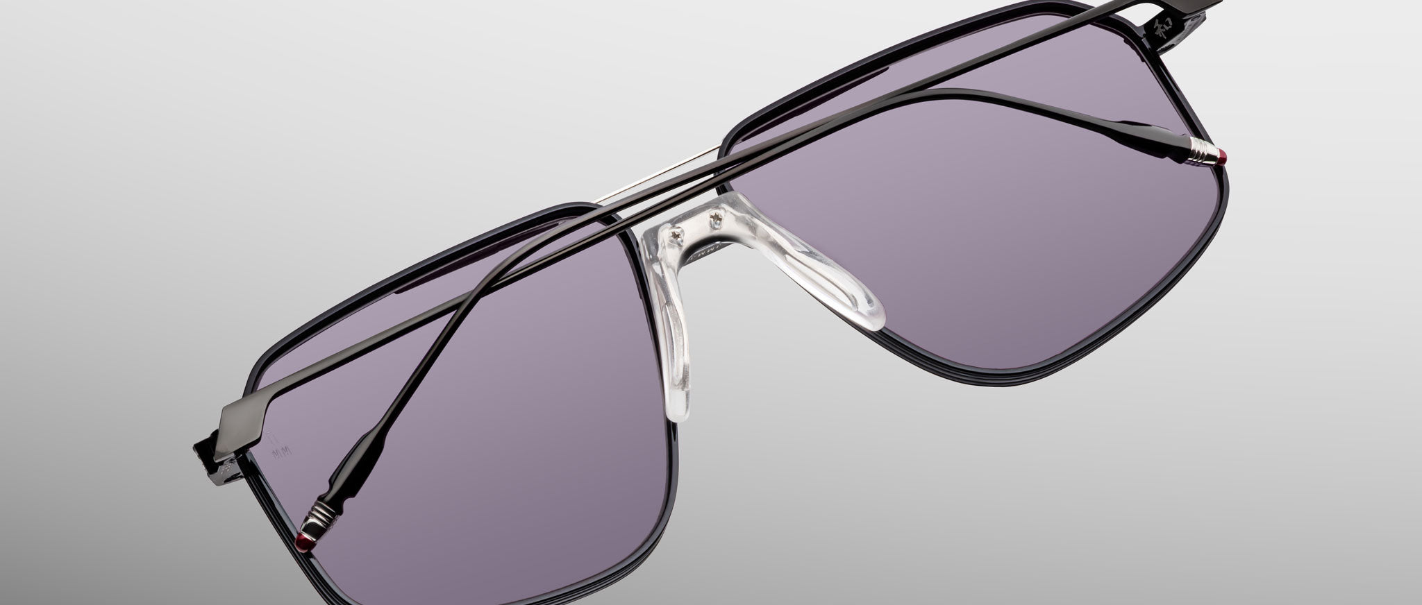 The Jacques Marie Mage Jagger by Jacques Marie Mage is a pair of oversized aviator sunglasses with a black beta titanium metal frame and purple-tinted lenses, showcased on a light gray background.