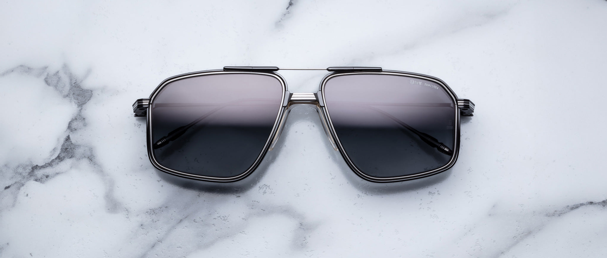 The Jacques Marie Mage Jagger sunglasses by Jacques Marie Mage, featuring black square beta titanium metal frames, rest on a white marble surface.