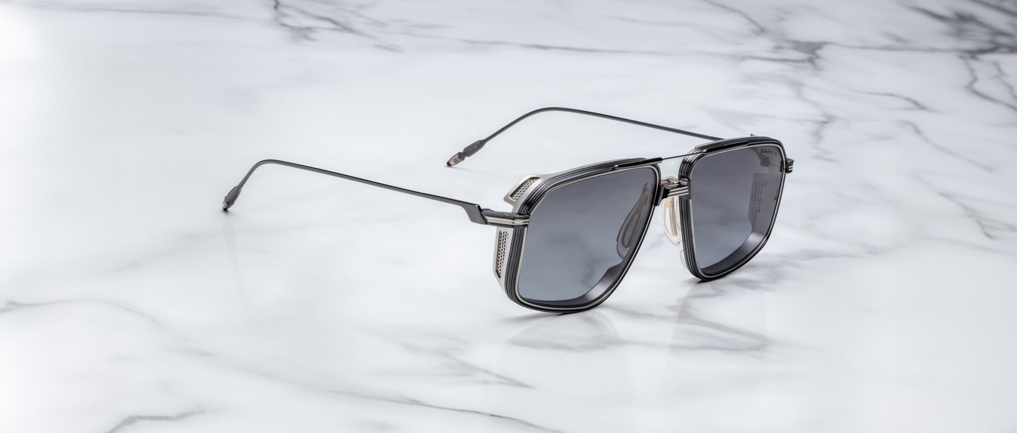 The Jacques Marie Mage Jagger by Jacques Marie Mage are modern black oversized aviator sunglasses with metallic temple detailing, crafted from beta titanium, displayed on a white marble surface.