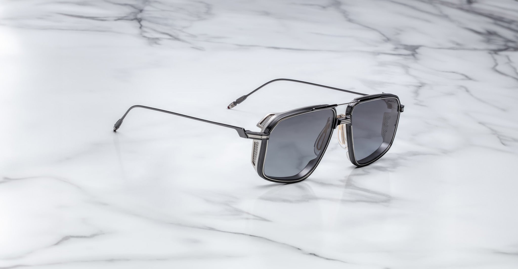 The Jacques Marie Mage Jagger by Jacques Marie Mage are modern black oversized aviator sunglasses with metallic temple detailing, crafted from beta titanium, displayed on a white marble surface.