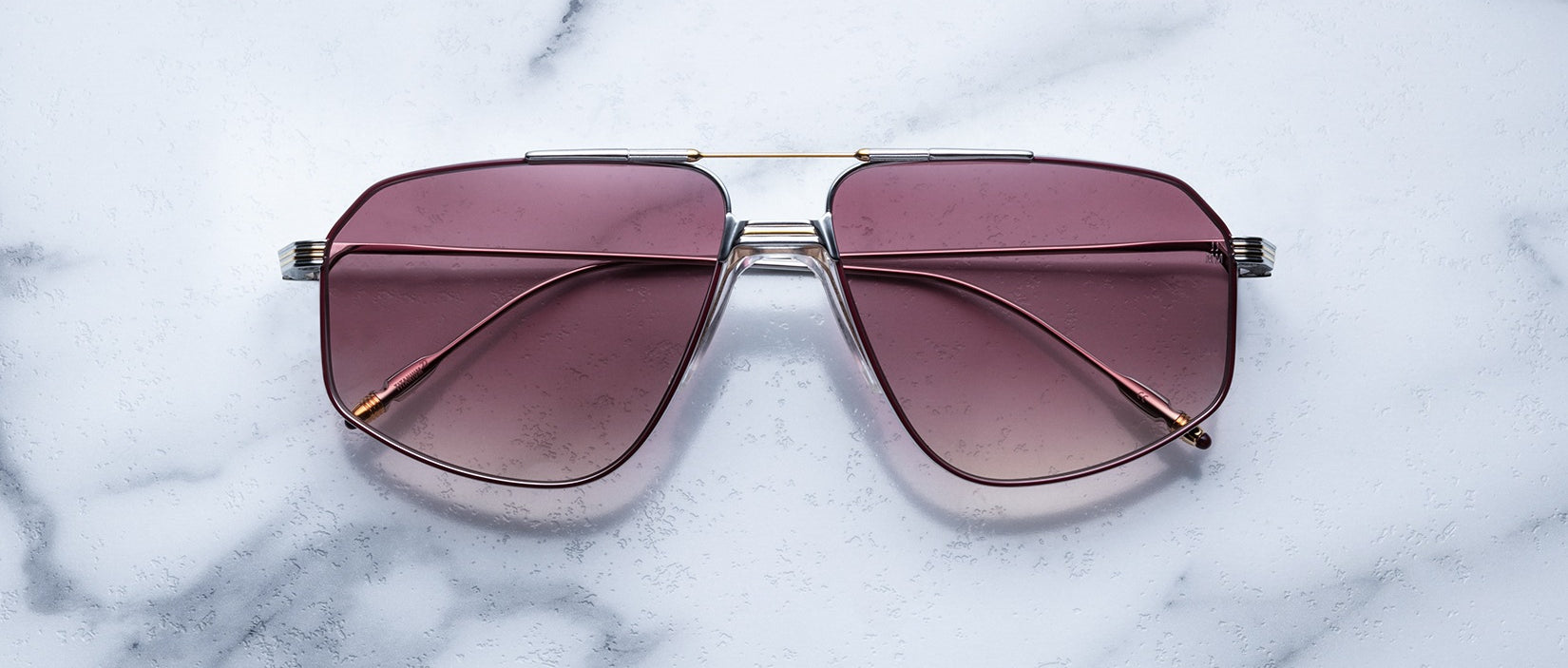 The Jacques Marie Mage Jagger sunglasses feature an oversized aviator design with pink-tinted lenses and a silver beta titanium frame, shown here on a white marble surface.