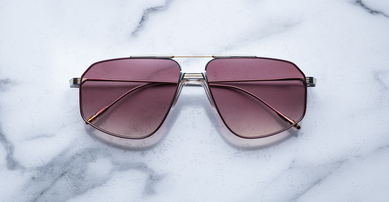 The Jacques Marie Mage Jagger sunglasses feature an oversized aviator design with pink-tinted lenses and a silver beta titanium frame, shown here on a white marble surface.