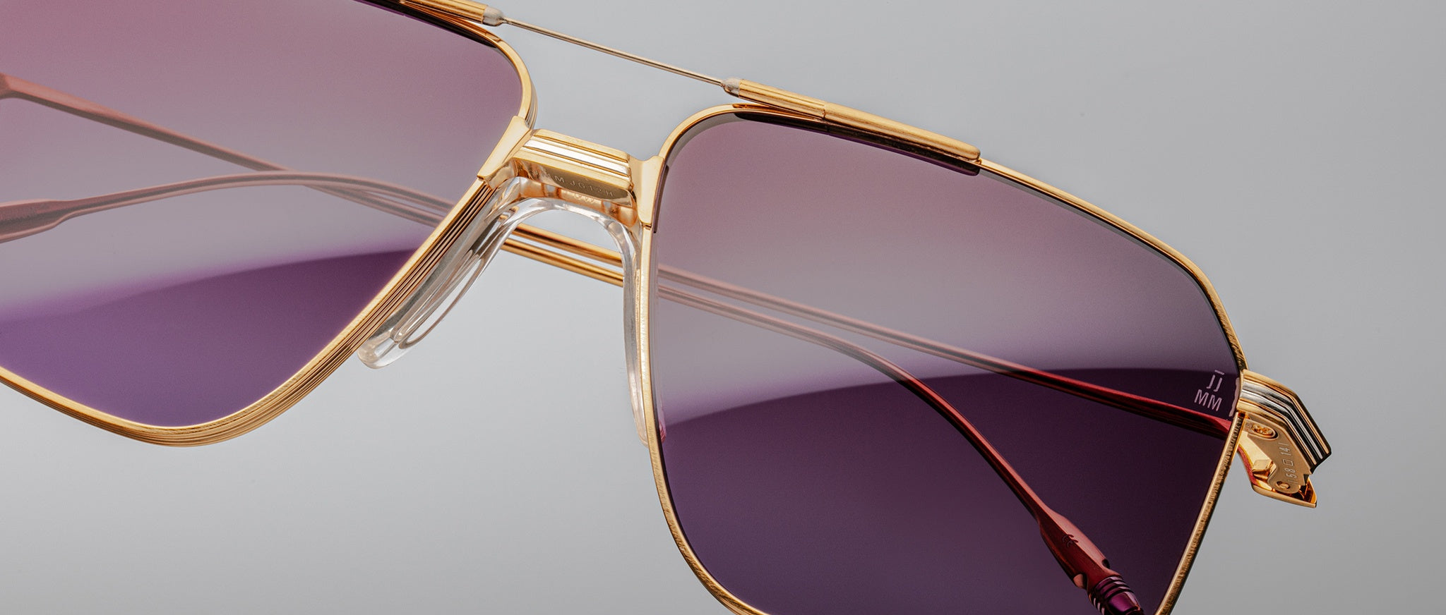 Close-up of Jacques Marie Mage Jagger oversized aviator sunglasses by Jacques Marie Mage, featuring gold frames and purple gradient lenses, displayed against a plain gray background.