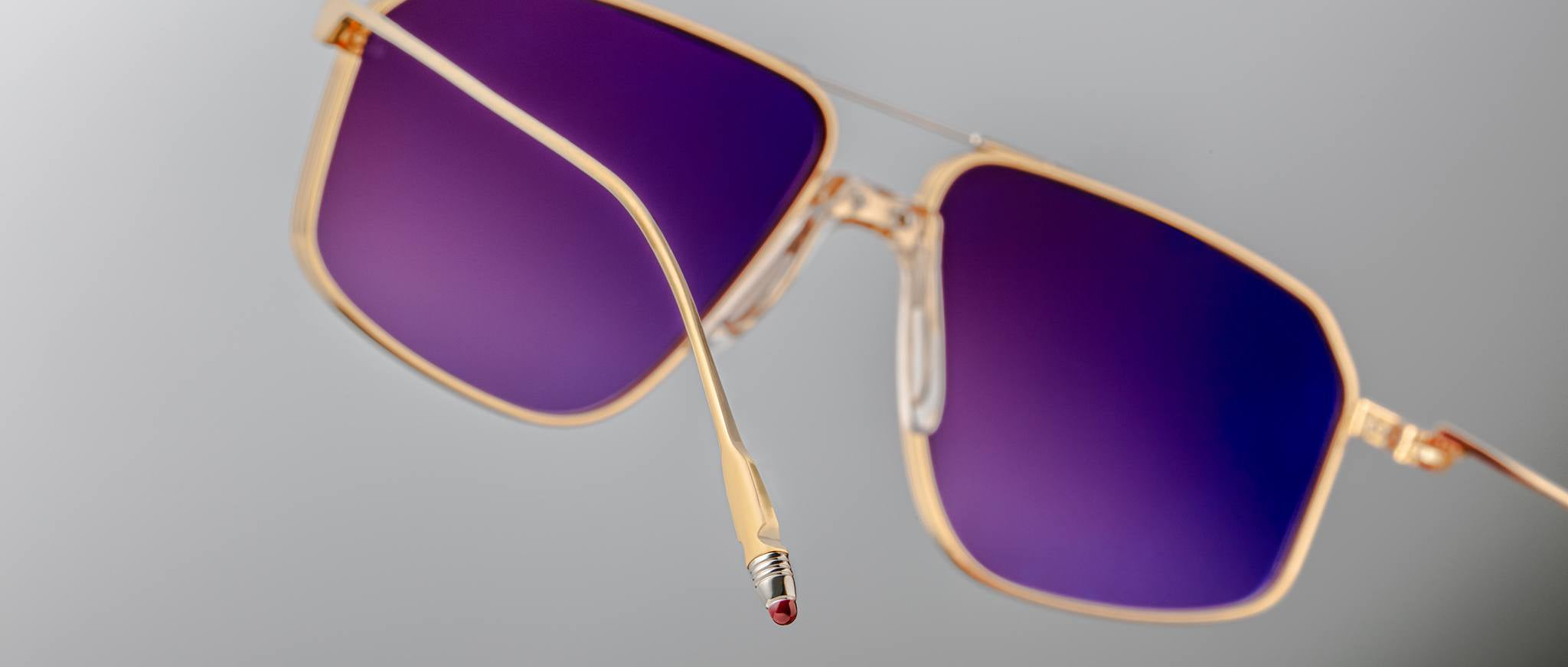 Jacques Marie Mage Jagger sunglasses feature gold beta titanium oversized aviator frames with square purple-tinted lenses and a quirky pencil eraser tip on the left arm, embodying the brand’s distinctive flair.