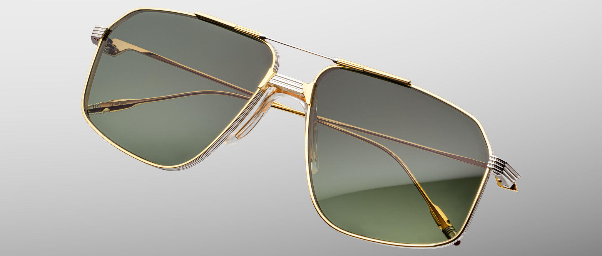 The Jacques Marie Mage Jagger oversized aviator sunglasses by Jacques Marie Mage feature gold rims and green-tinted lenses in beta titanium, displayed against a plain light gray background.