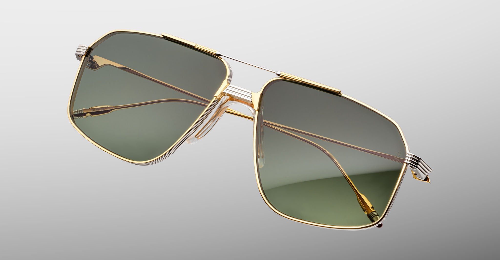 The Jacques Marie Mage Jagger oversized aviator sunglasses by Jacques Marie Mage feature gold rims and green-tinted lenses in beta titanium, displayed against a plain light gray background.