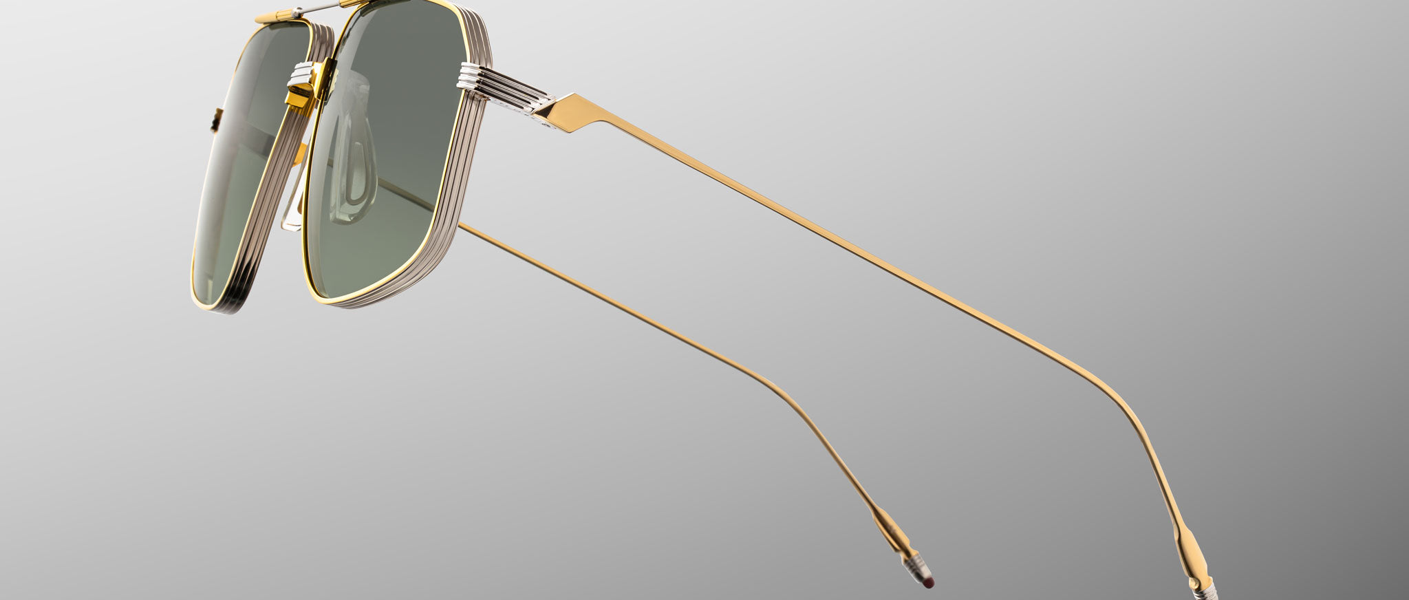 The Jacques Marie Mage Jagger by Jacques Marie Mage features gold-framed, rectangular sunglasses inspired by oversized aviators, crafted from beta titanium with green-tinted lenses, shown on a grey gradient background.