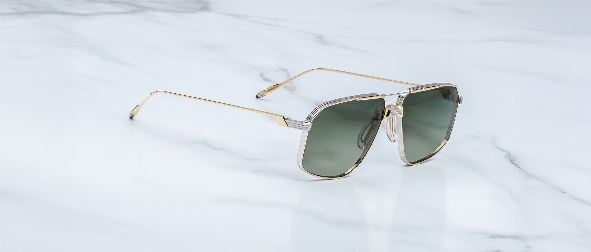 The Jacques Marie Mage Jagger sunglasses by Jacques Marie Mage feature oversized gold aviator frames and dark lenses, elegantly displayed on a white marble surface.