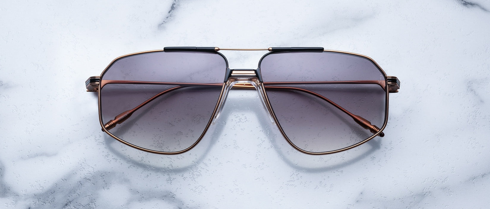 The Jacques Marie Mage Jagger sunglasses feature oversized aviator-style brown gradient lenses and slim beta titanium frames by Jacques Marie Mage, displayed on a white marble surface.