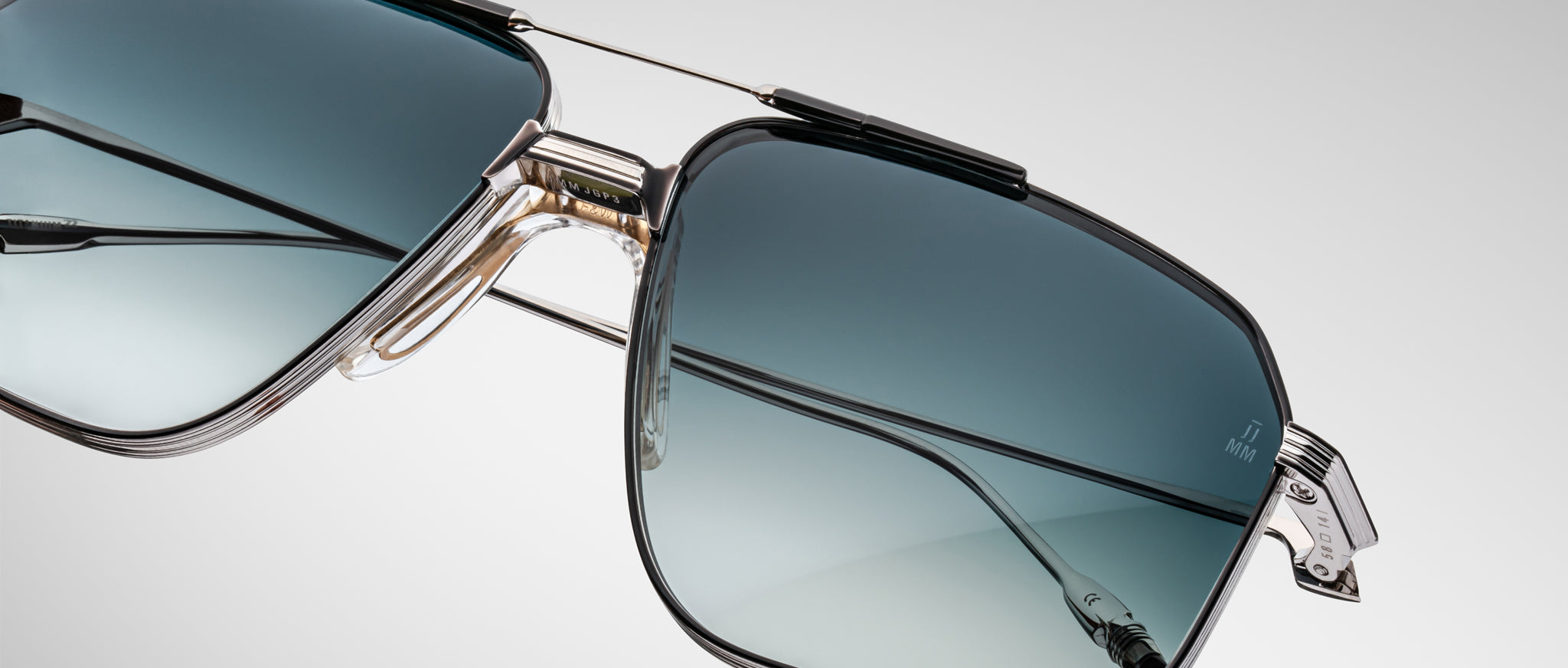 Close-up of Jacques Marie Mage Jagger sunglasses, featuring an oversized aviator design with blue gradient lenses, a silver beta titanium frame, and transparent nose pads against a plain light background.