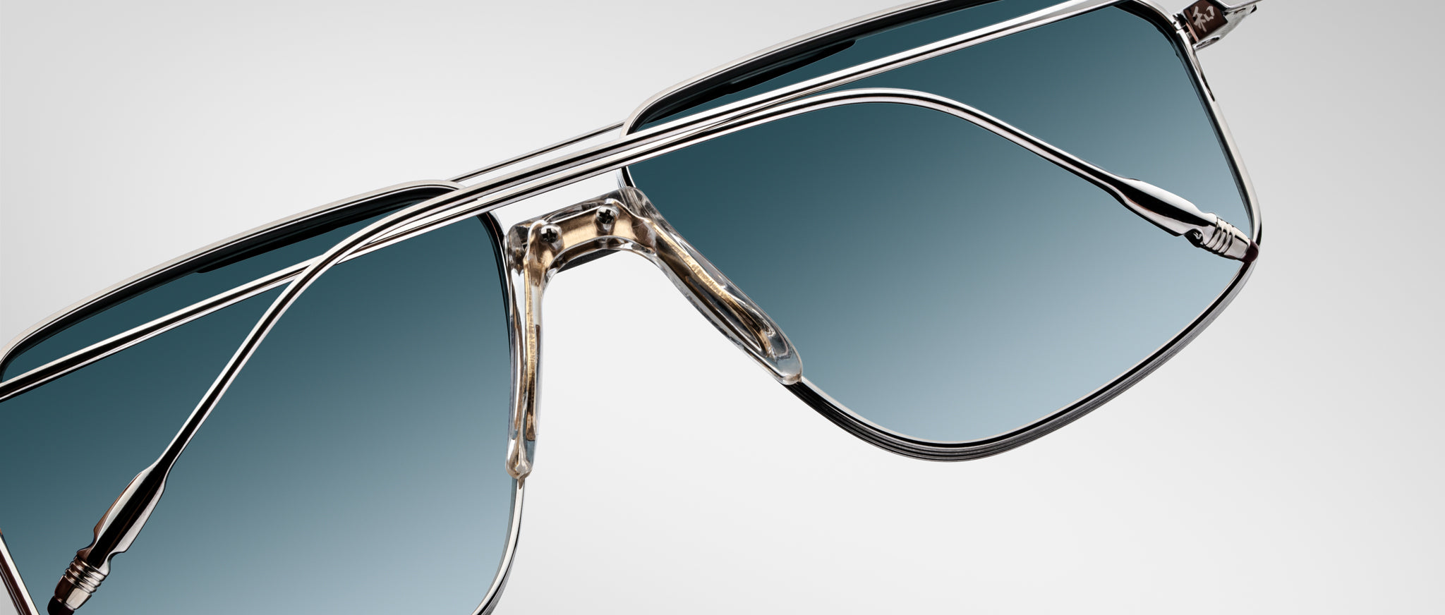 Close-up of Jacques Marie Mage Jagger aviator sunglasses by Jacques Marie Mage, featuring oversized sleek beta titanium frames and blue gradient lenses on a light gray background.
