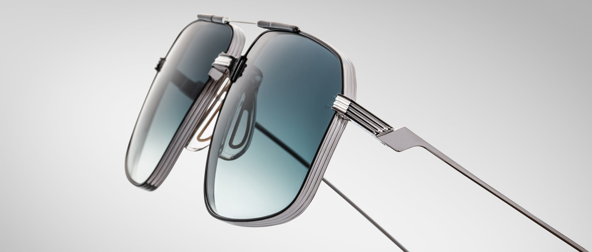 Close-up of Jacques Marie Mage Jagger sunglasses by Jacques Marie Mage, showcasing oversized aviator style with a sleek metallic frame and gradient blue lenses against a plain light gray background.