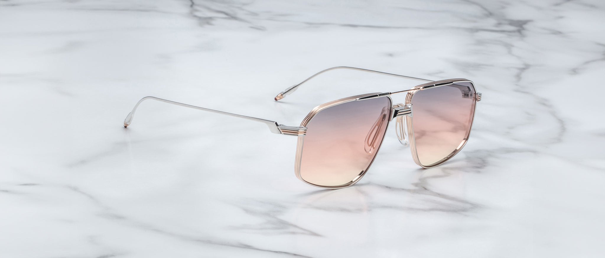 A pair of Jacques Marie Mage Jagger oversized aviator sunglasses with pink gradient lenses and thin beta titanium frames from Jacques Marie Mage, elegantly displayed on a white marble surface.