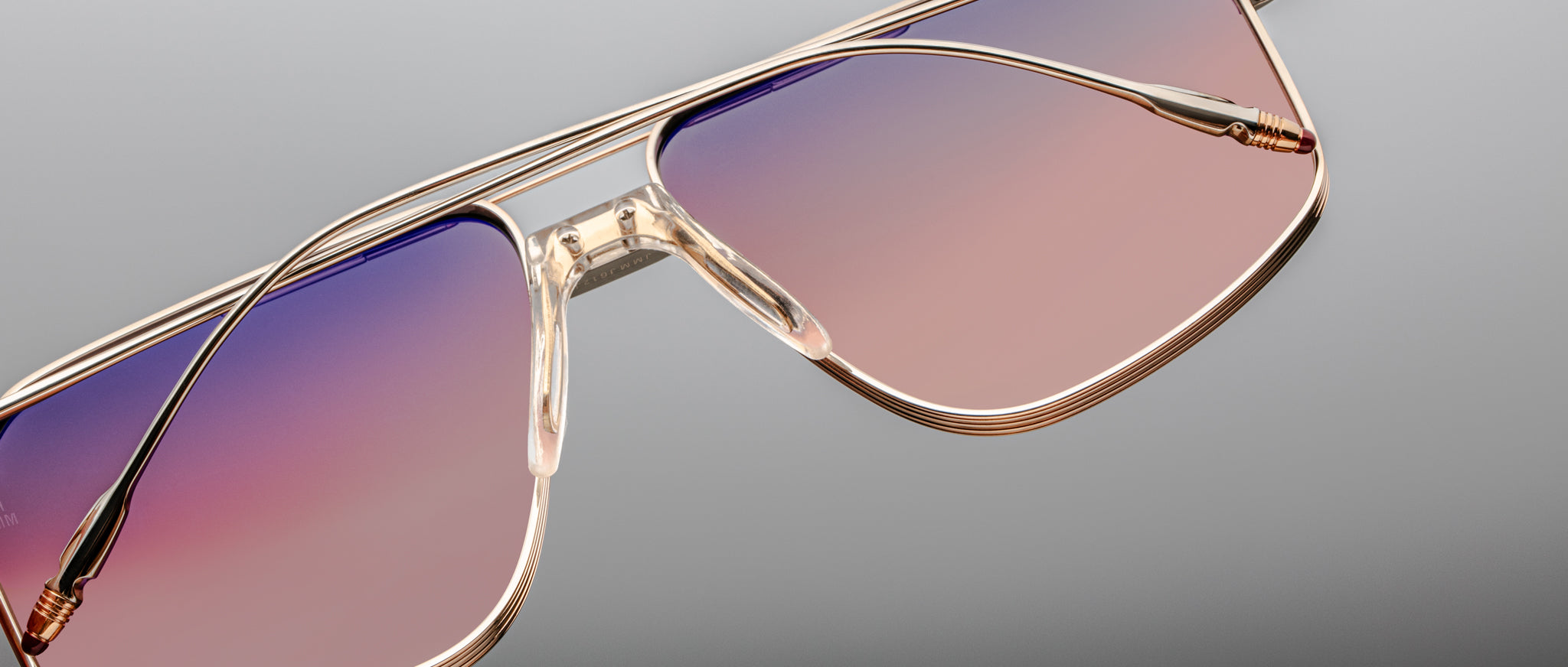 Close-up of Jacques Marie Mage Jagger oversized aviator sunglasses with gold frames and gradient pink to purple lenses, set against a light gray background.