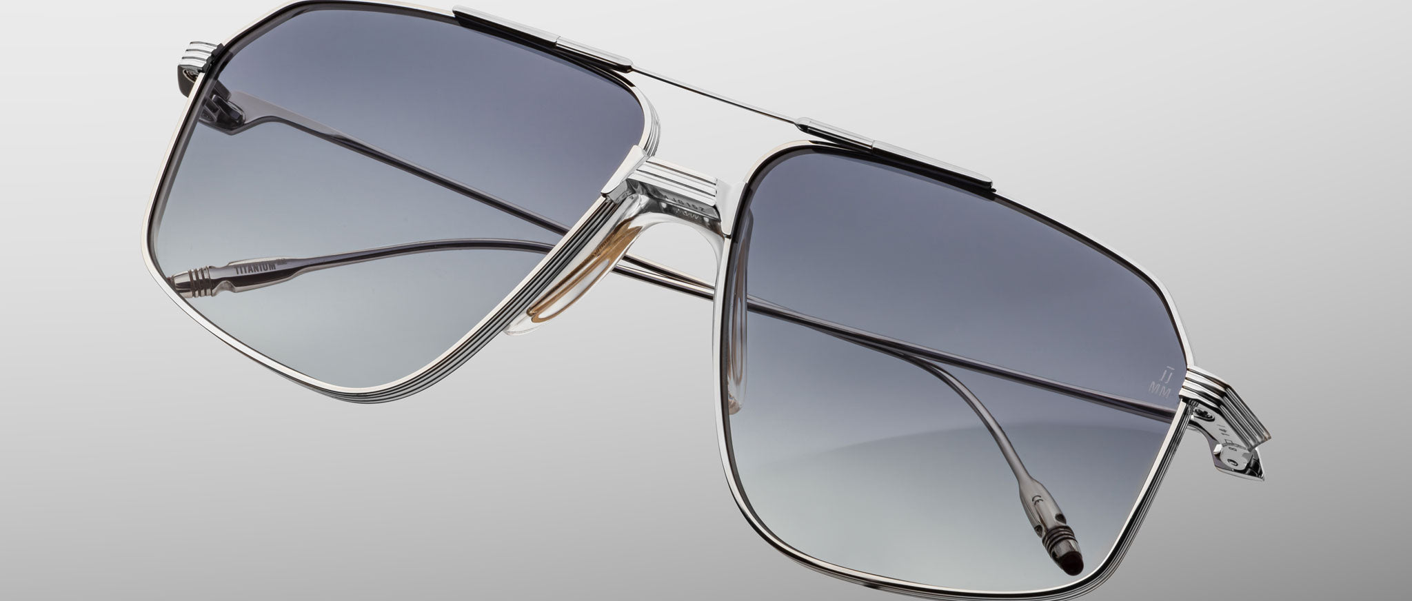 The Jacques Marie Mage Jagger sunglasses by Jacques Marie Mage feature silver oversized aviator frames in beta titanium with gradient gray lenses, inspired by the iconic Jagger style, displayed on a light gray background.
